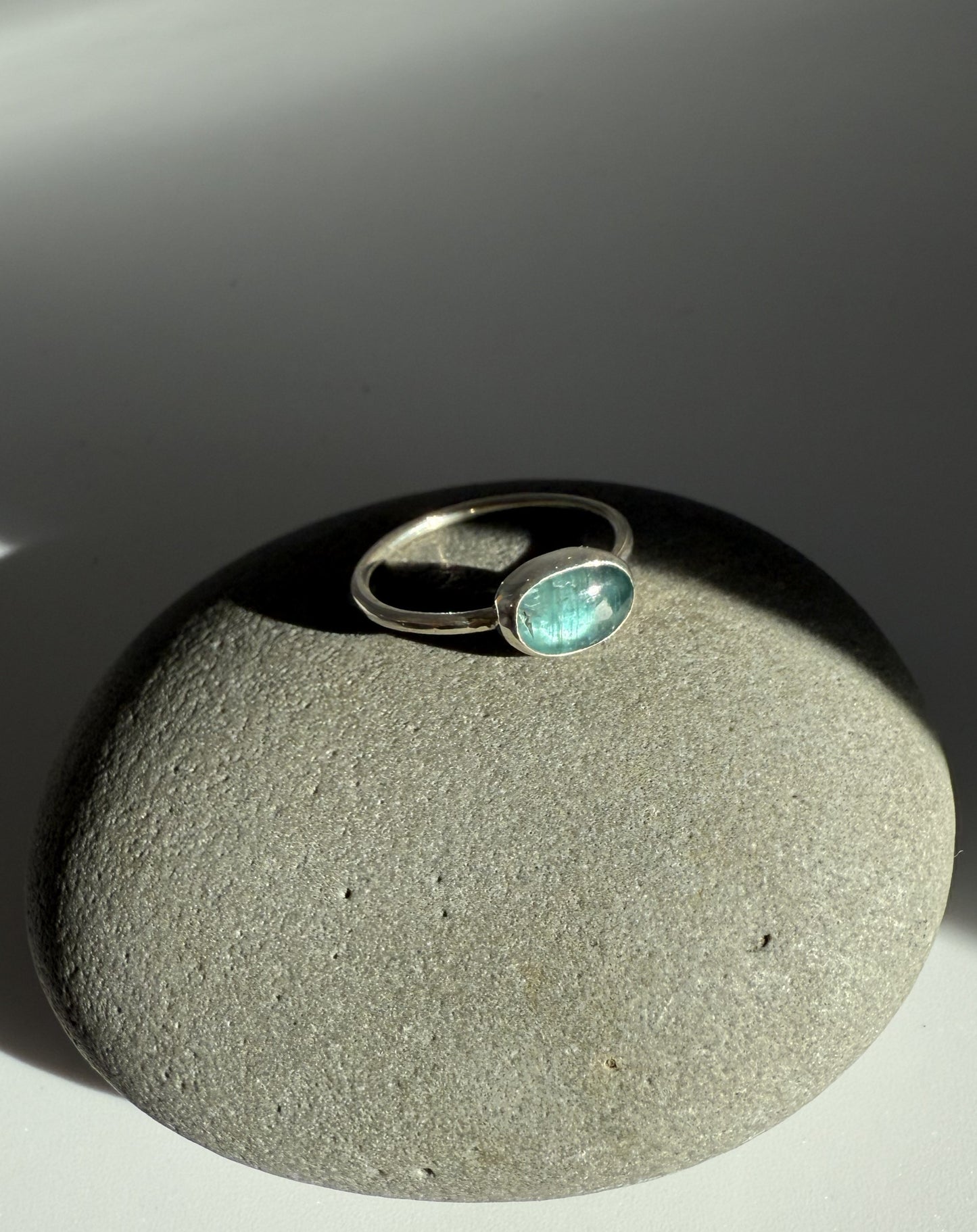 Silver ring with a green kyanite gemstone on a grey stone surface