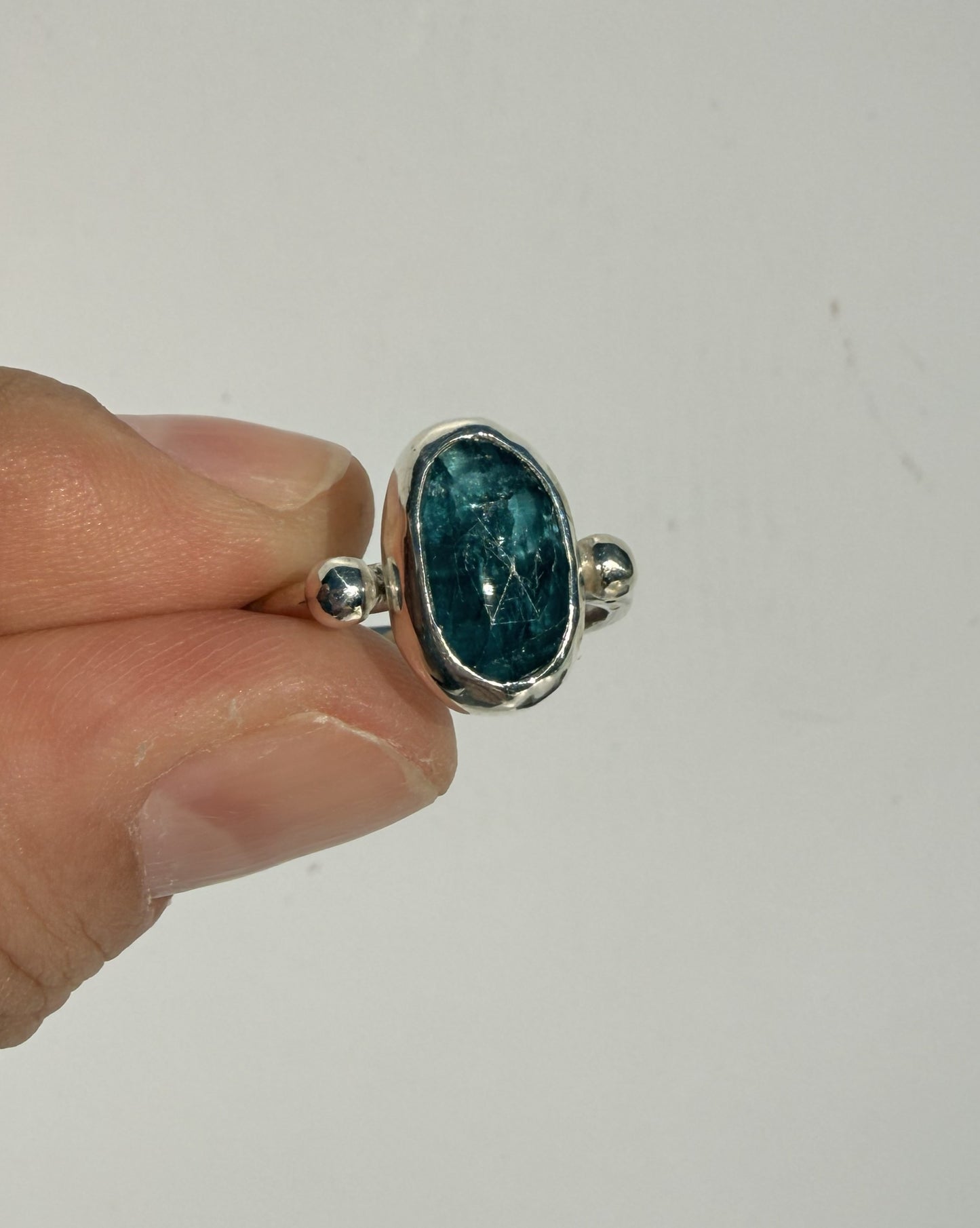 Silver ring with a blue kyanite gemstone held by a hand against a white background