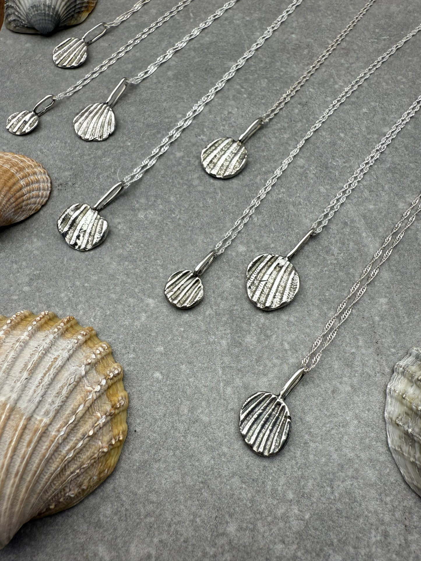 Silver necklace with shell pendant on a textured surface with seashells.