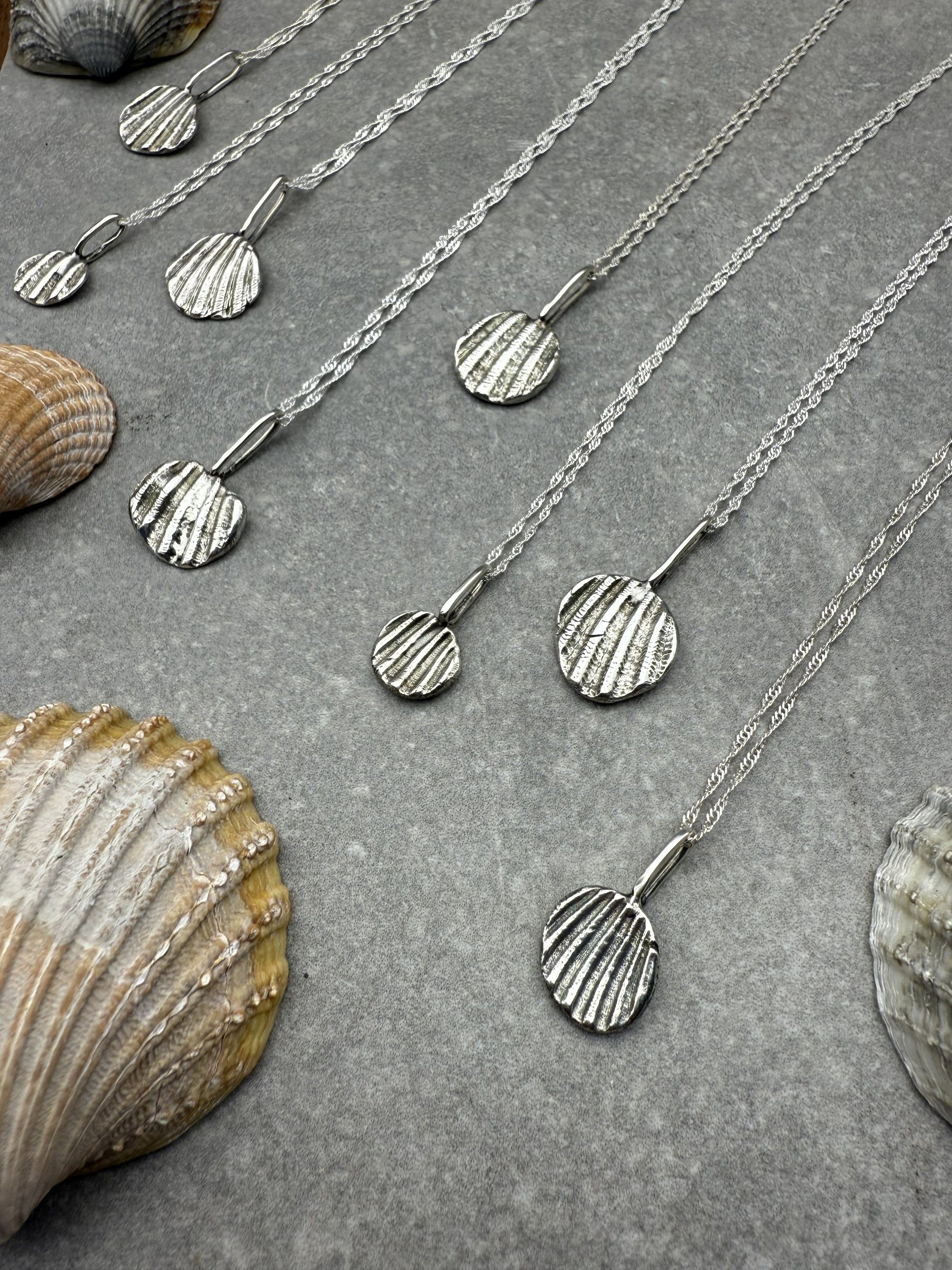 Silver necklace with shell pendant on a textured surface with seashells.