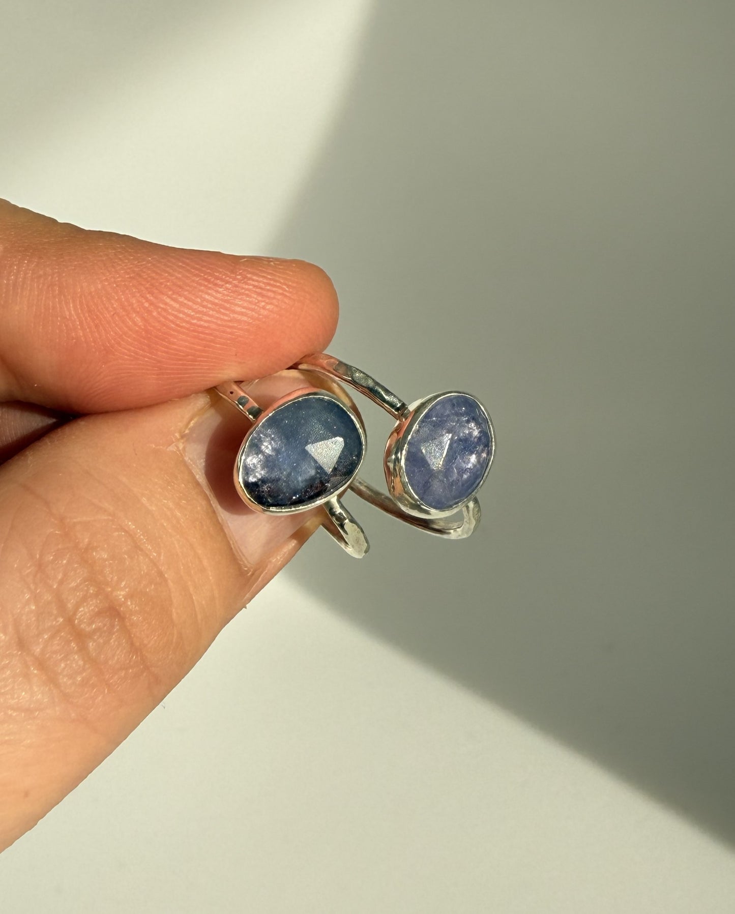 Silver ring with purple tanzanite gemstones held by a hand on a neutral background