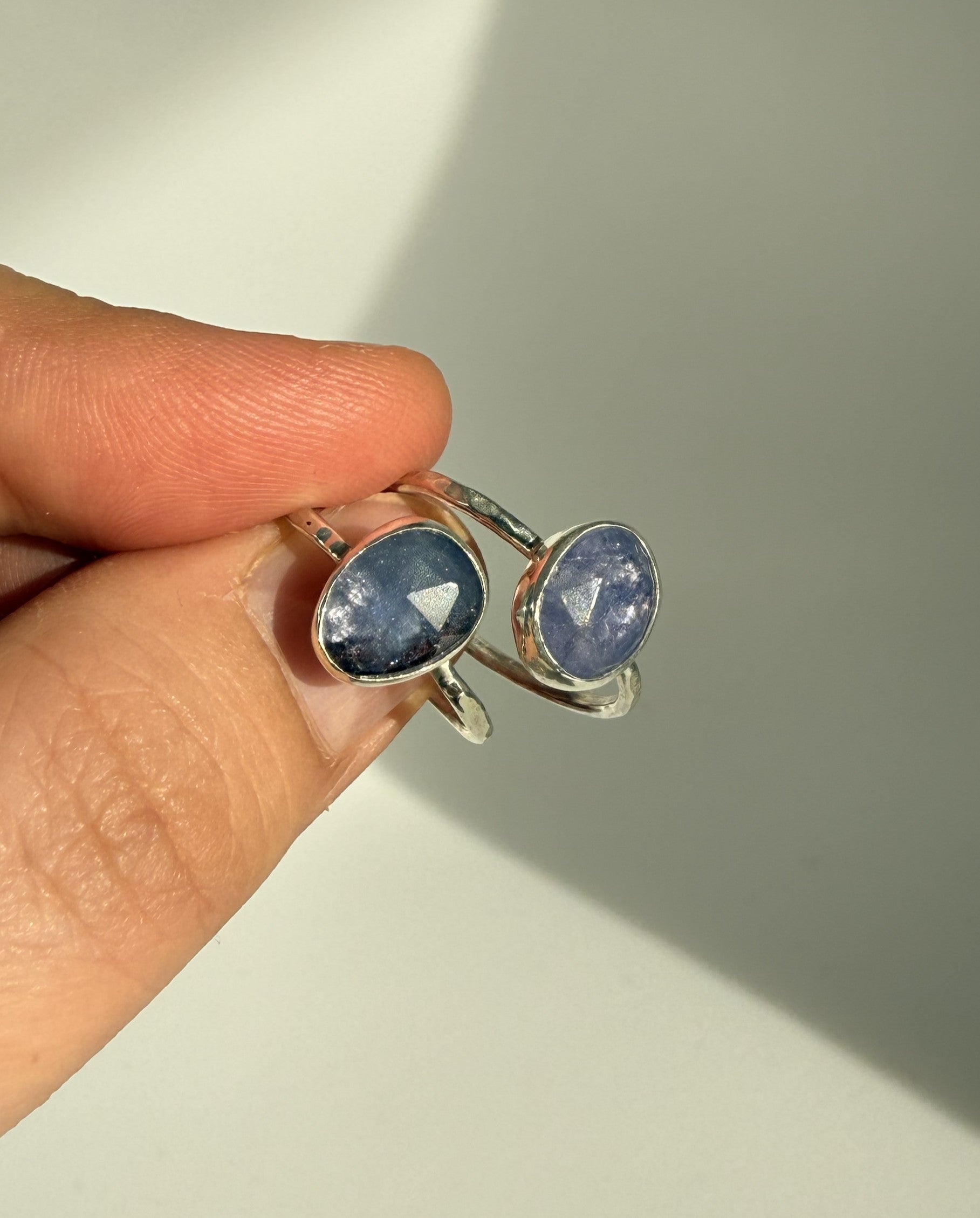 Silver ring with purple tanzanite gemstones held by a hand on a neutral background