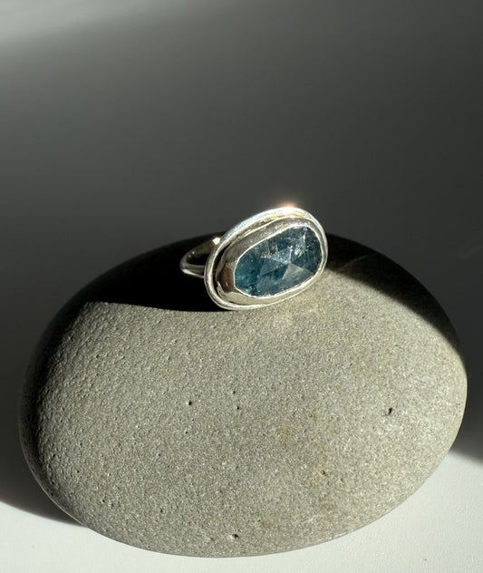 Silver ring with a teal kyanite gemstone on a grey stone surface