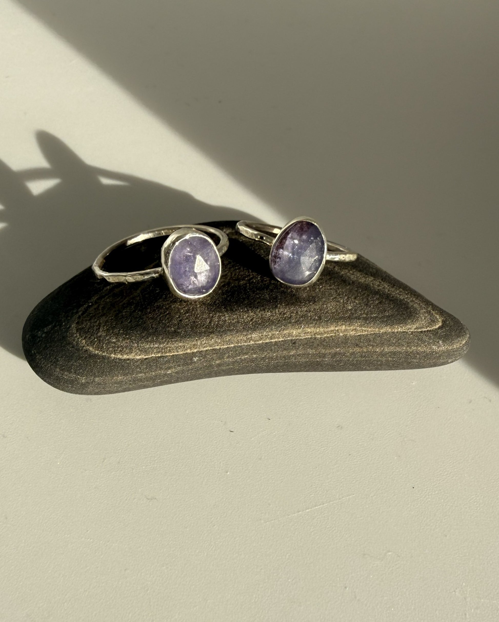 Pair of silver rings with purple tanzanite gemstones on a dark stone surface.