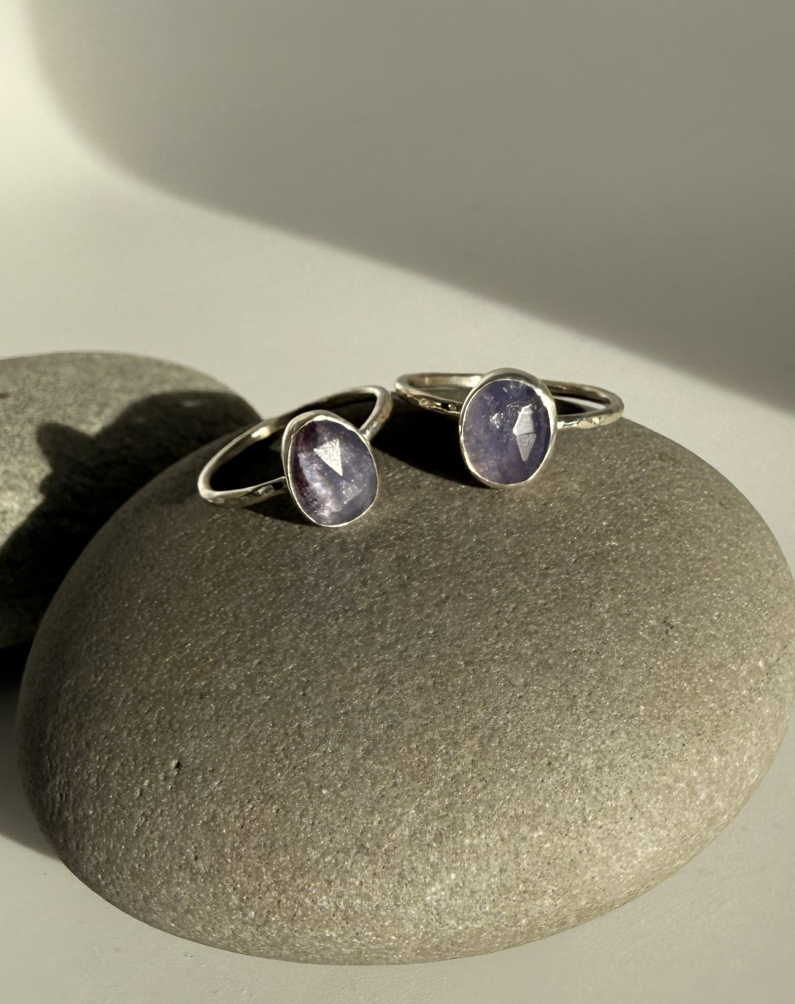 Two silver rings with purple tanzanite gemstones on a textured beige surface