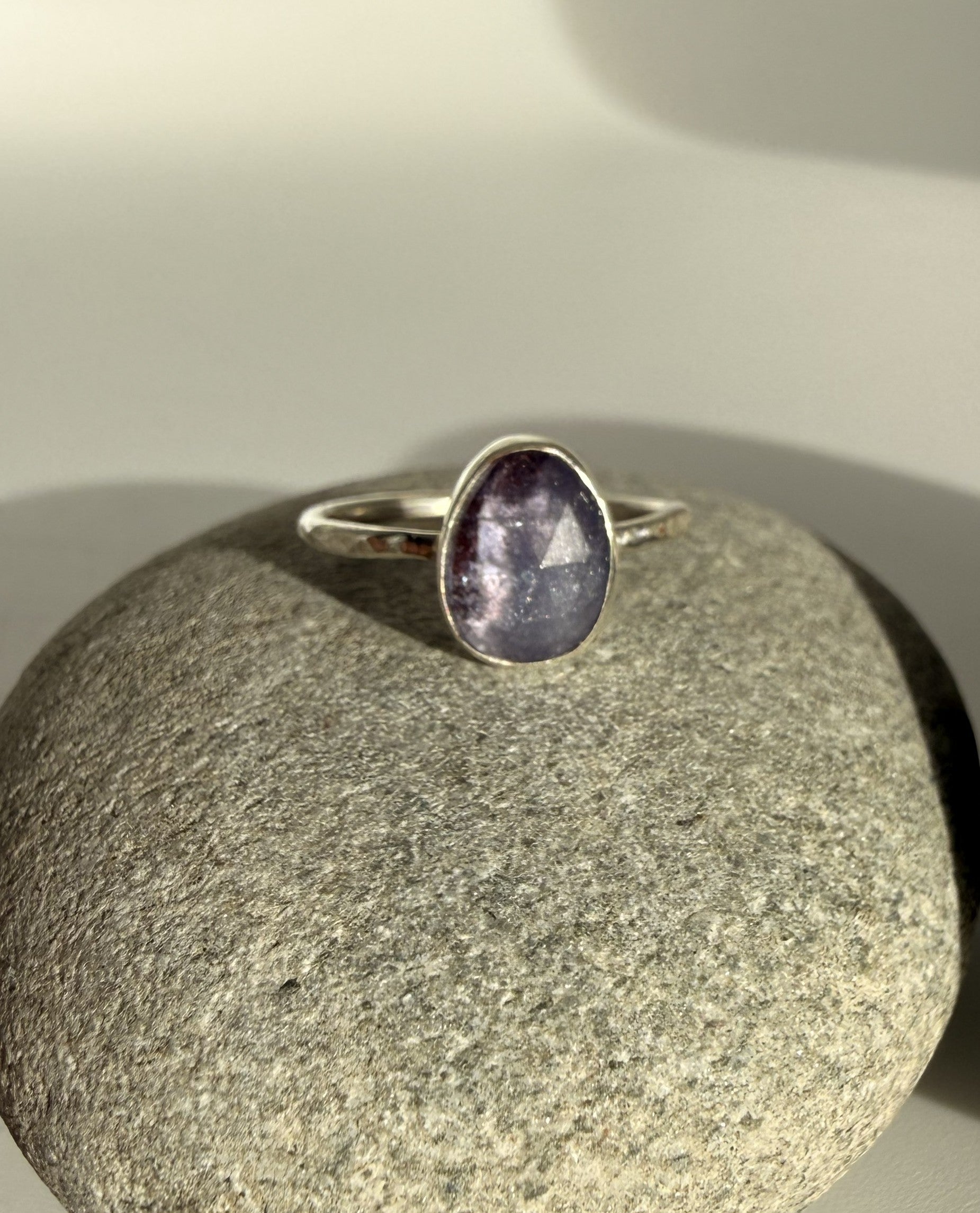 Silver ring with a purple tanzanite stone on a gray stone surface