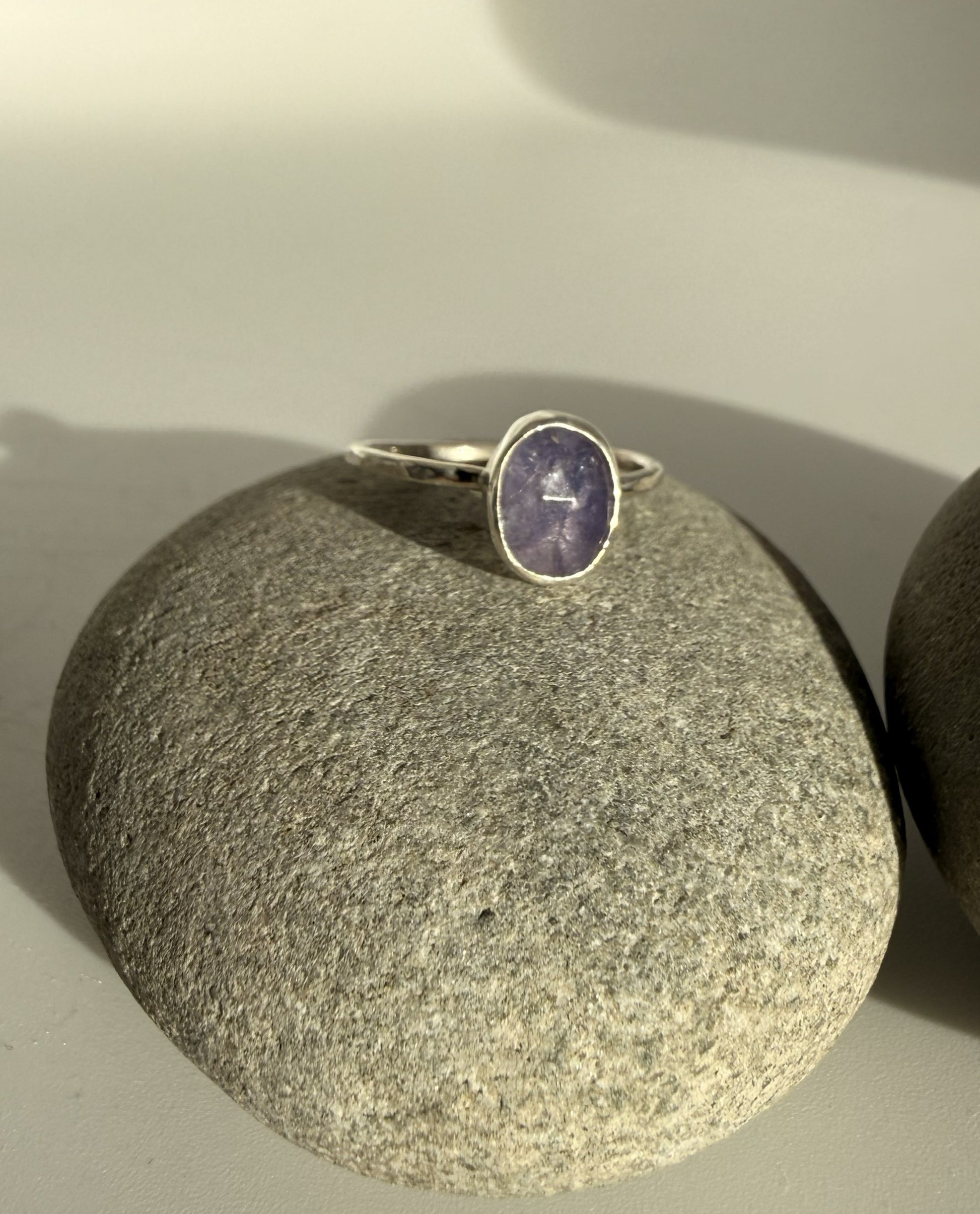 Silver ring with a purple tanzanite stone on a grey stone surface