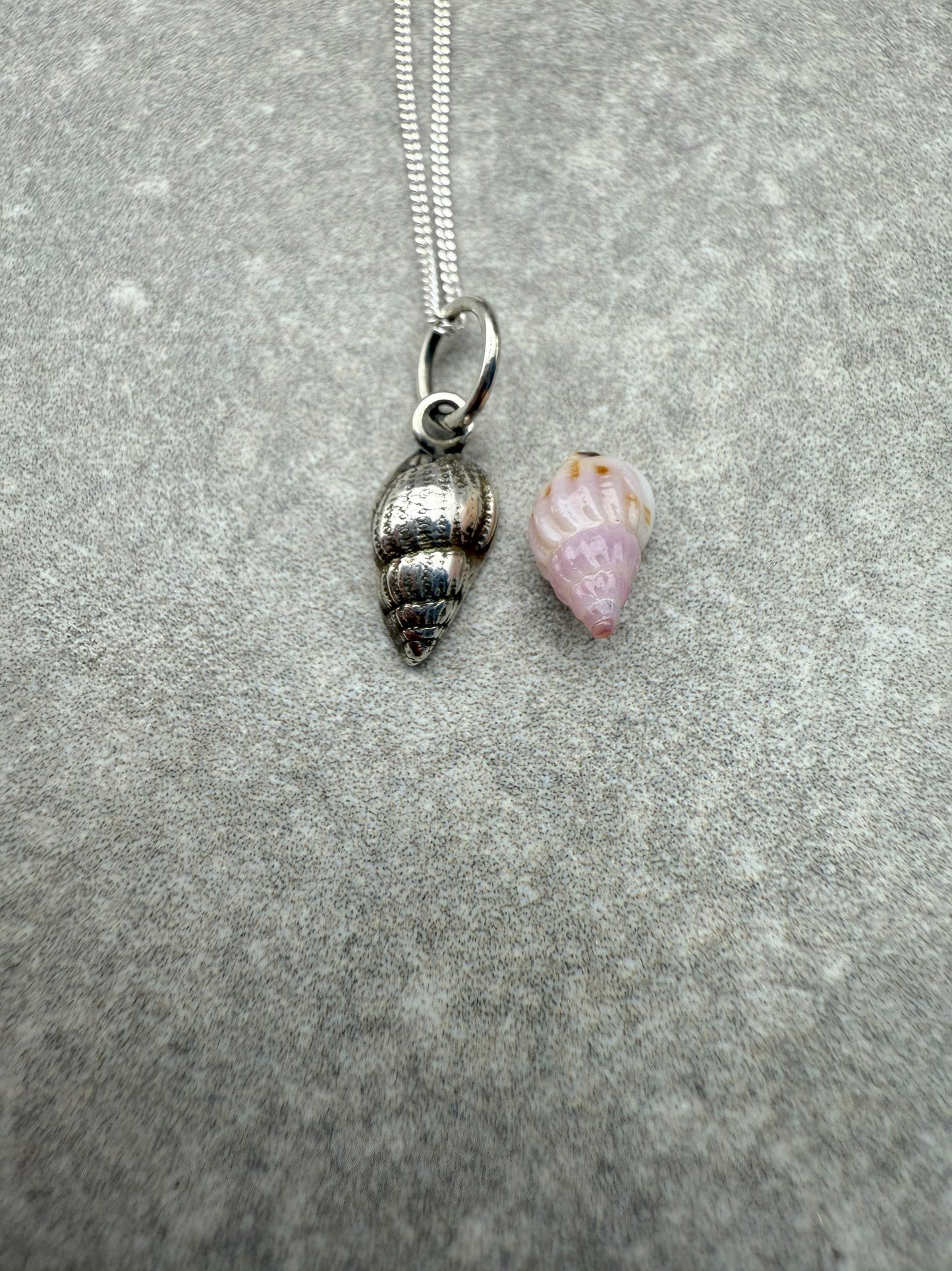 Silver shell pendant and pink shell charm on a chain against a gray background