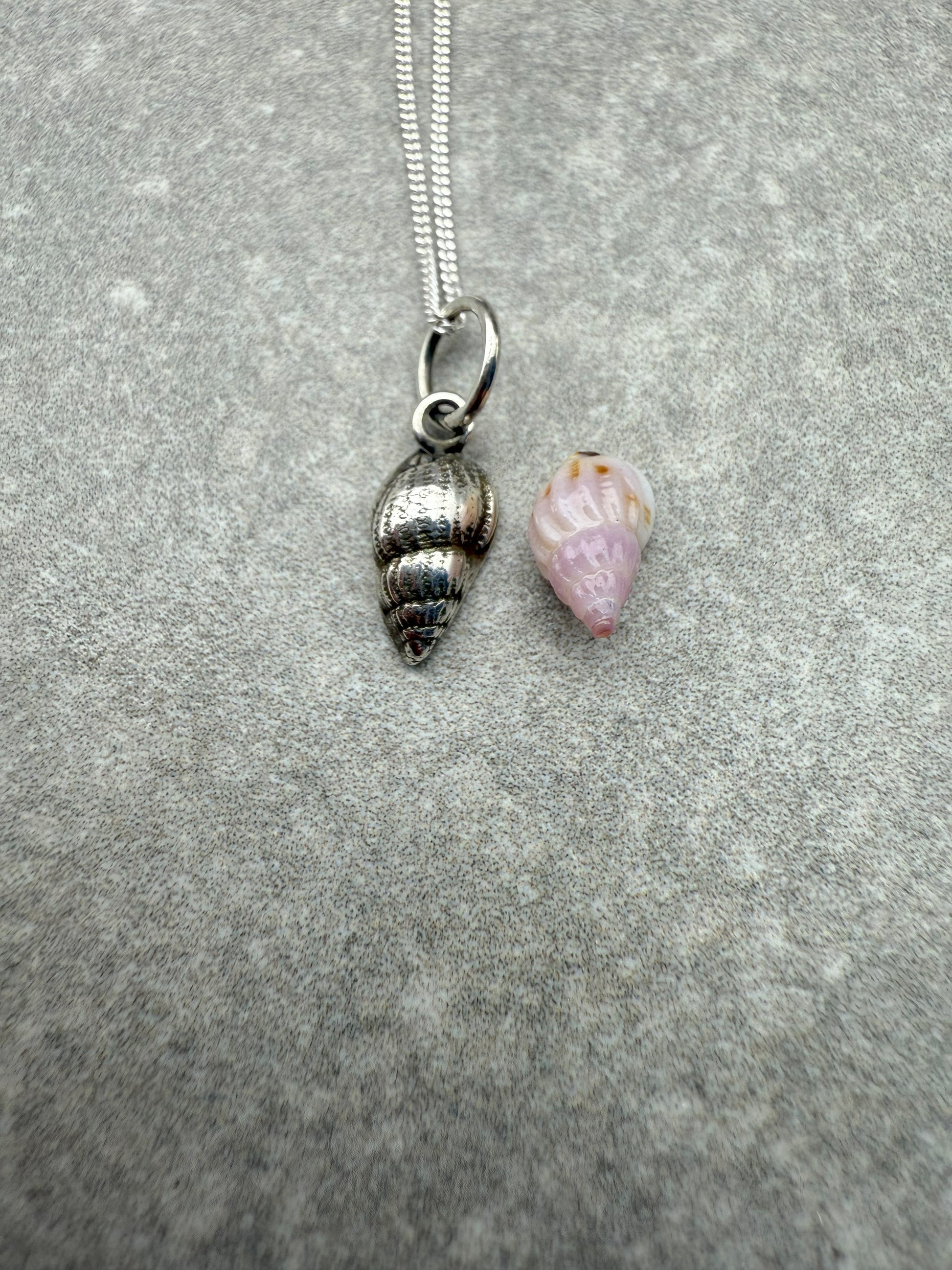 Silver shell pendant and pink shell charm on a chain against a gray background