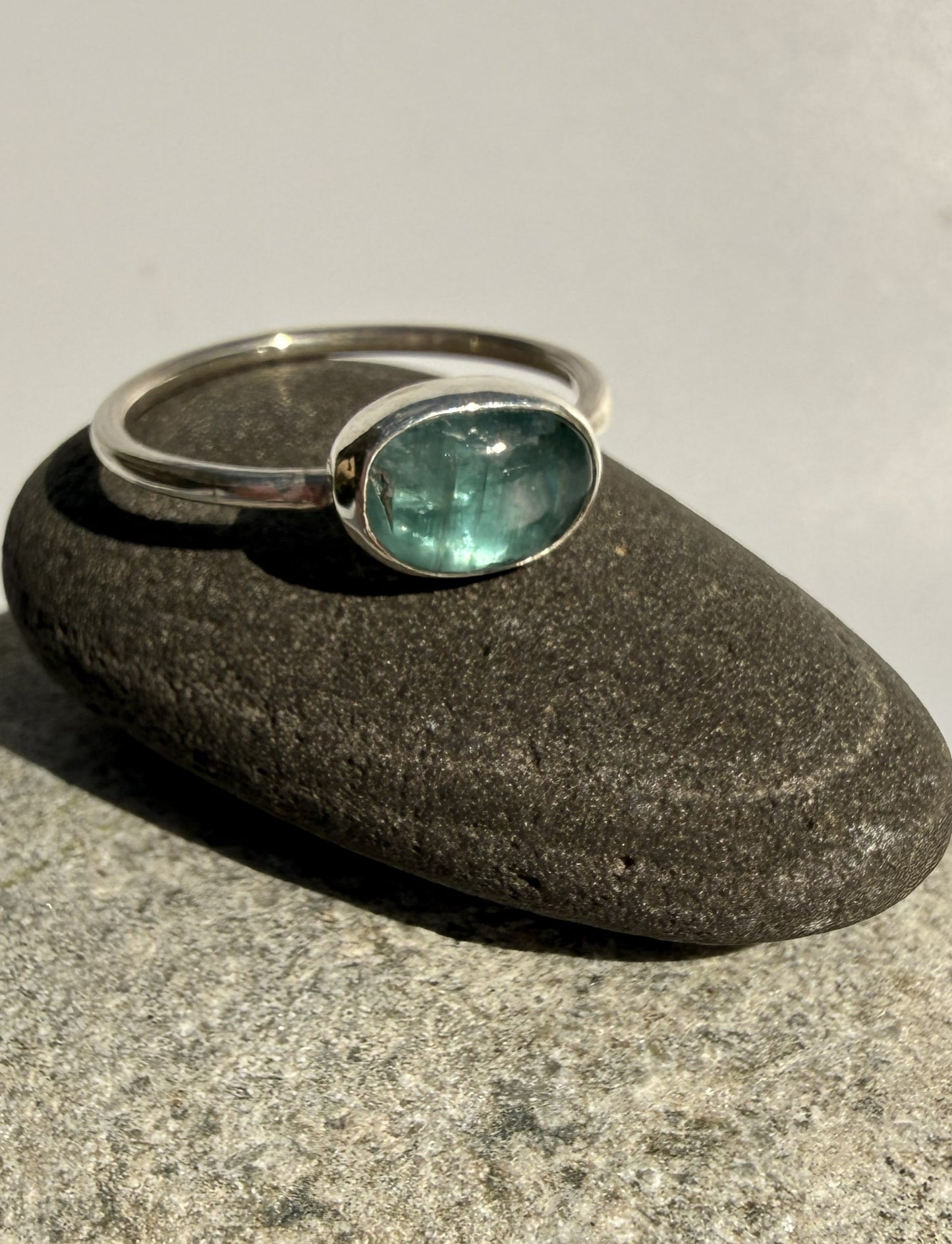 Silver ring with a green kyanite gemstone on a grey stone surface