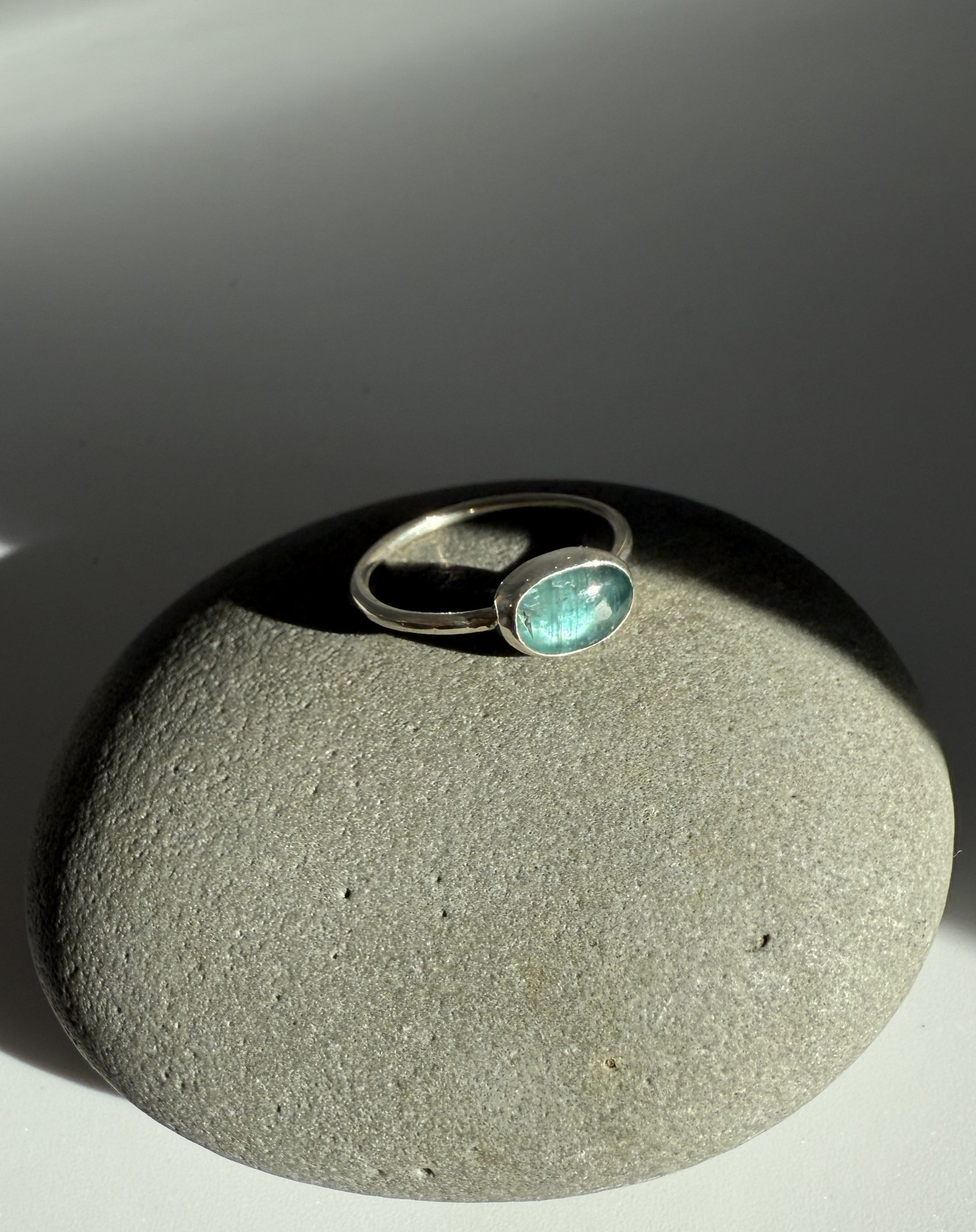 Silver ring with a green kyanite gemstone on a grey stone surface