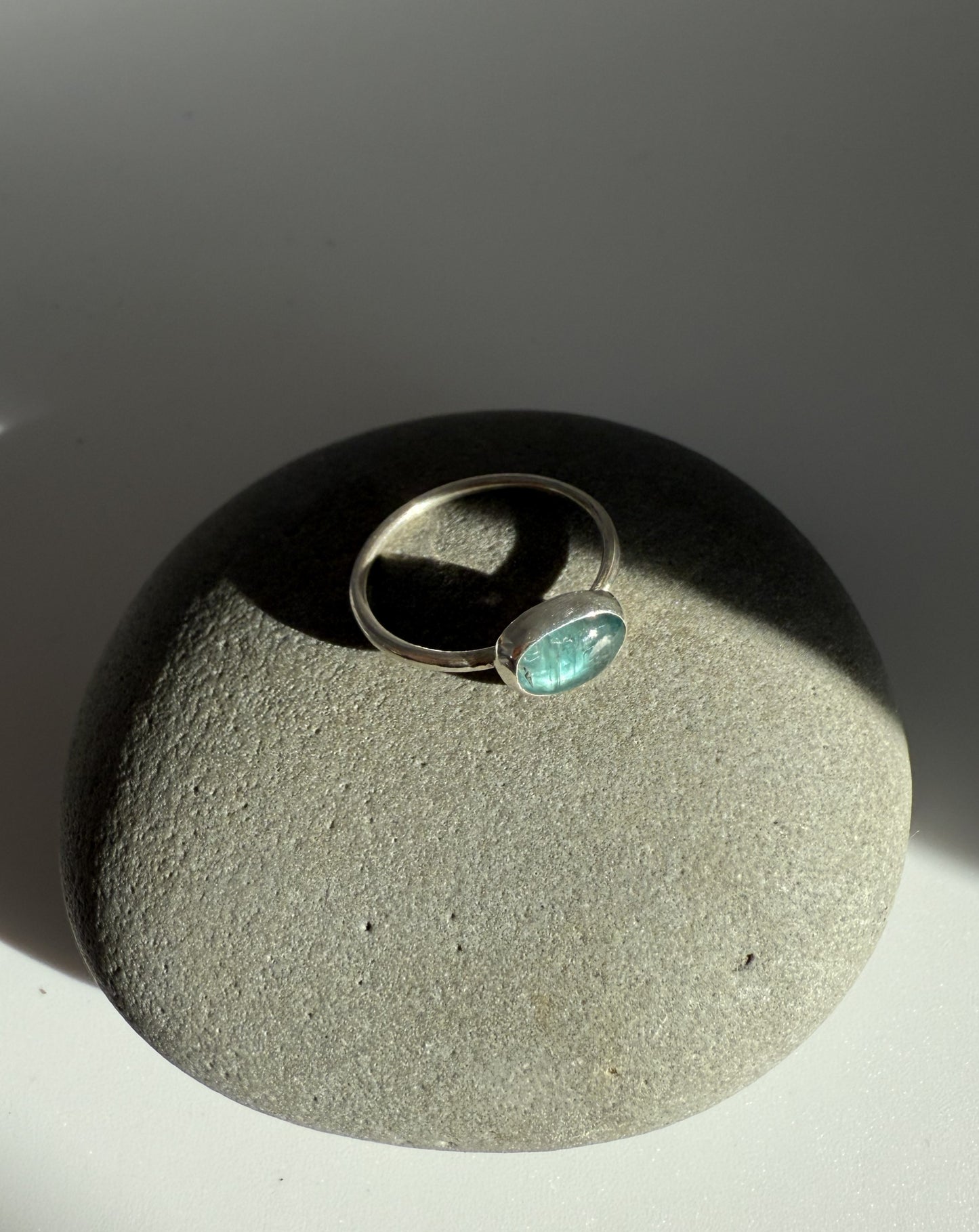 Silver ring with a green kyanite gemstone on a textured grey surface