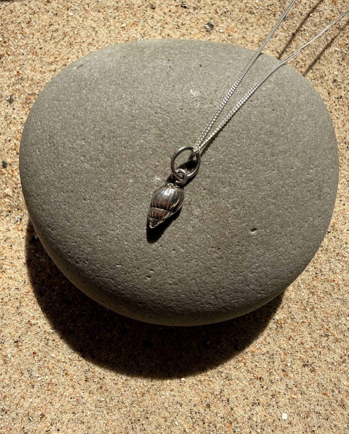 Silver shell pendant necklace on a gray stone with sand background