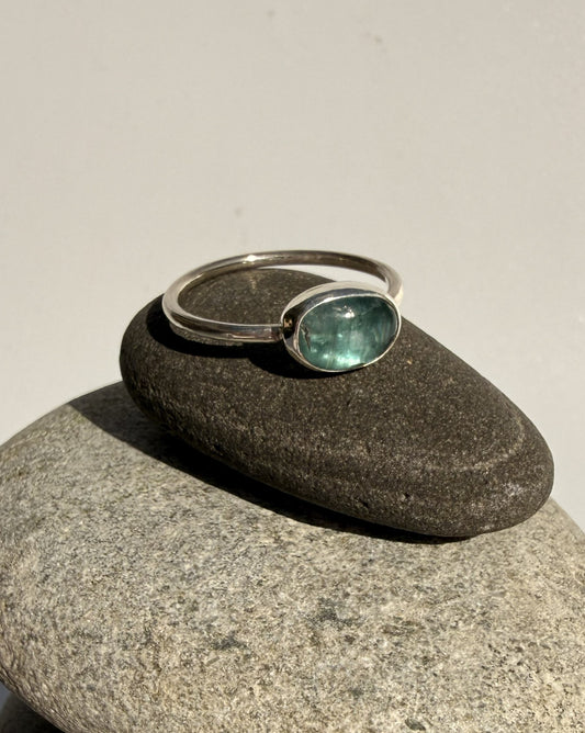Silver ring with a green kyanite gemstone on a grey stone surface