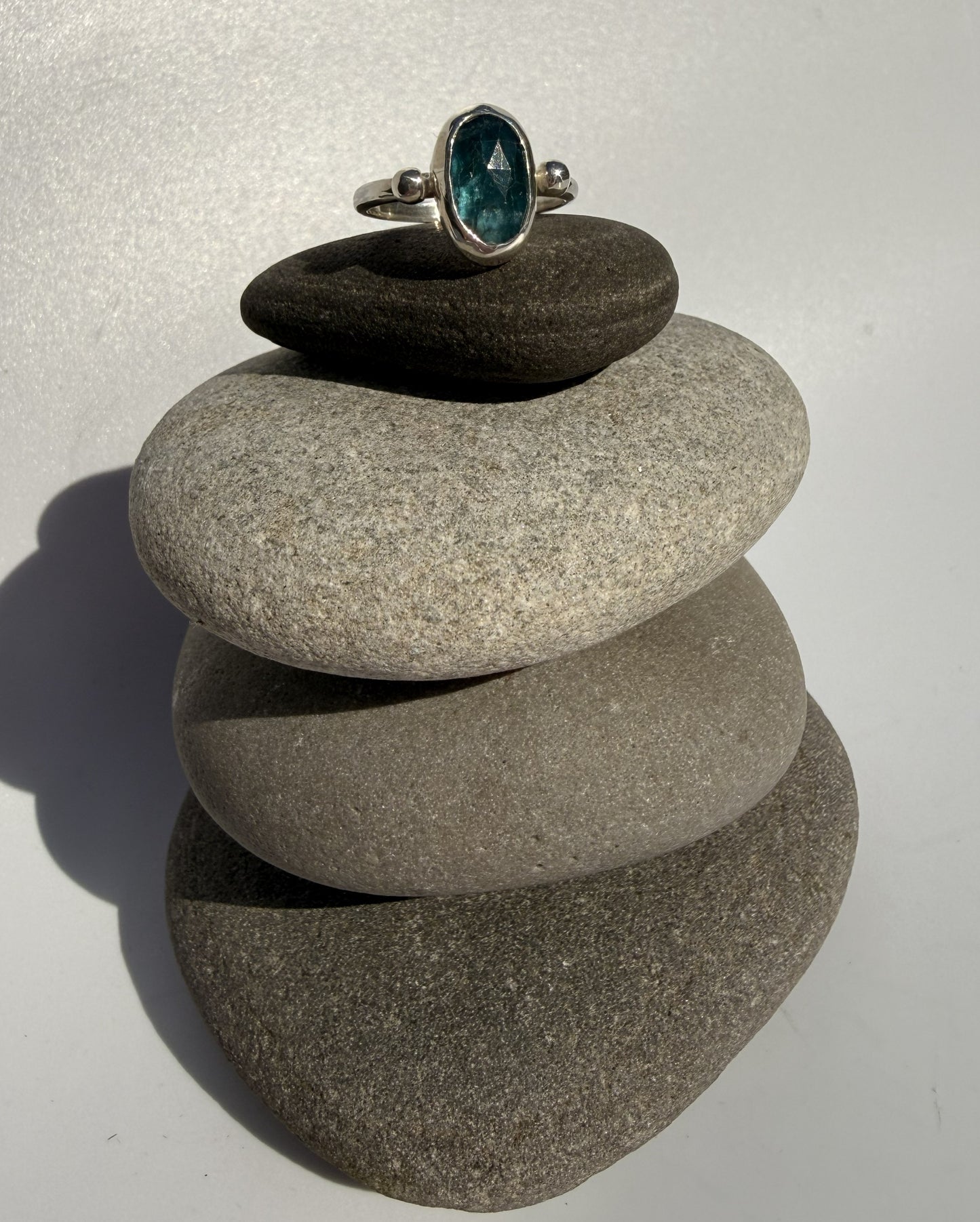Ring with a sea green kyanite gemstone on top of stacked stones against a white background