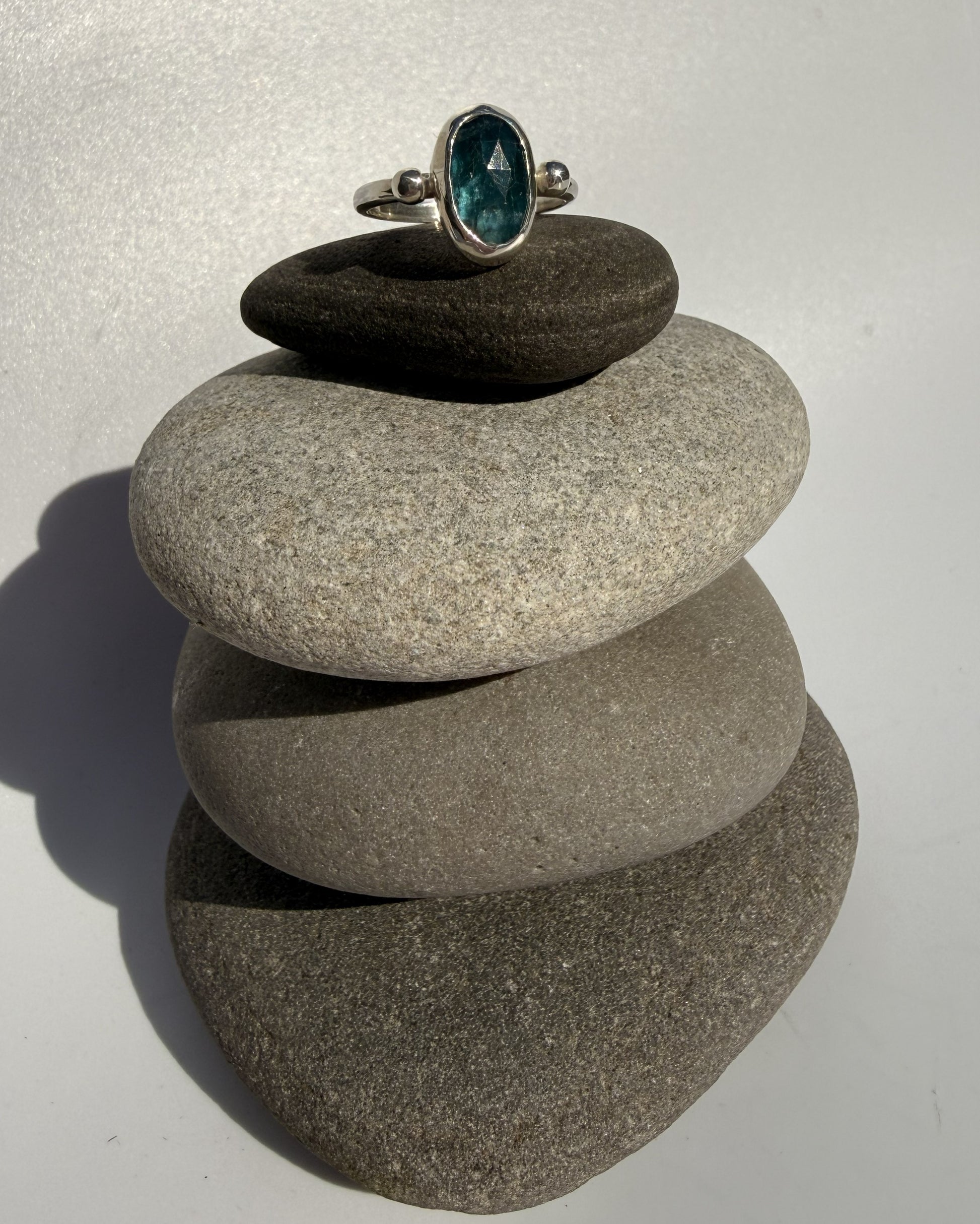 Ring with a sea green kyanite gemstone on top of stacked stones against a white background