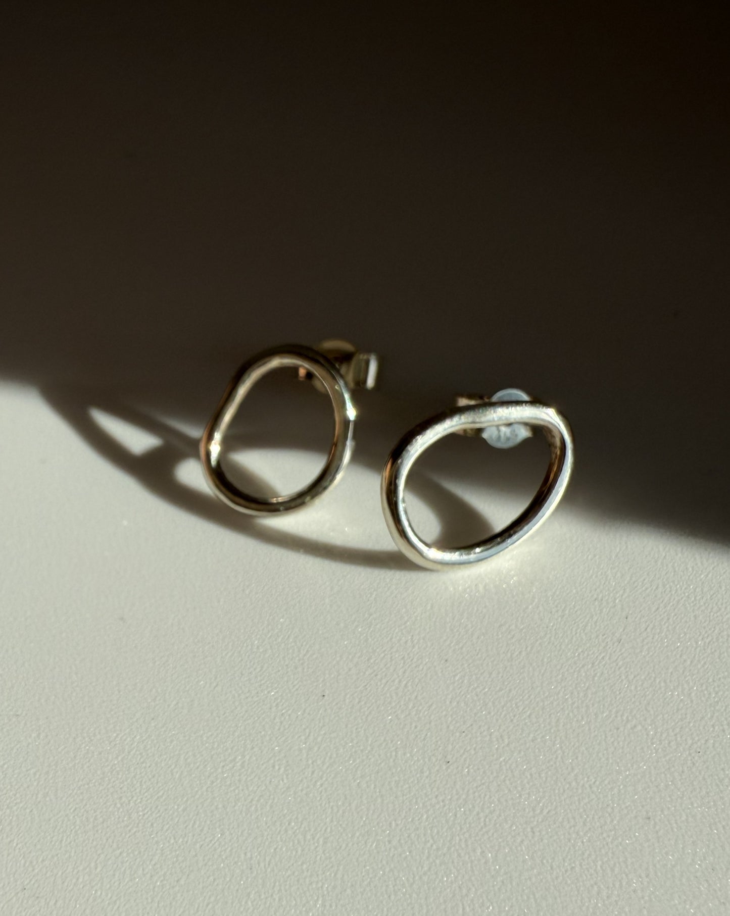 Pair of silver hoop stud earrings on a light surface with a dark background