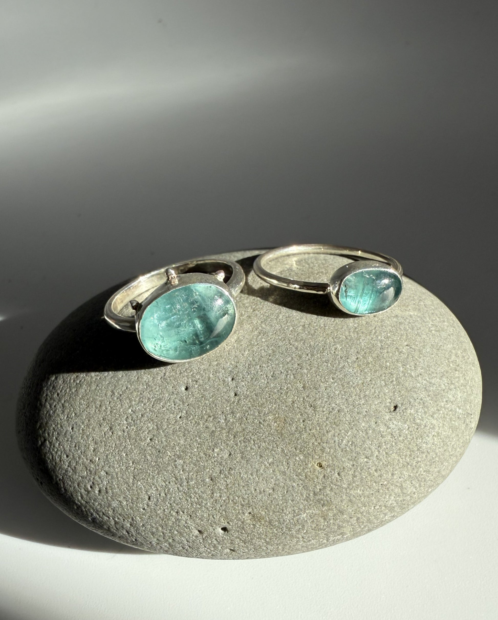 Silver rings with green kyanite gemstones on a stone surface