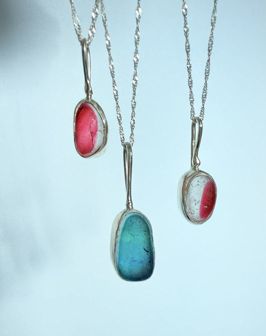 Three necklaces with sea glass pendants on a light blue background