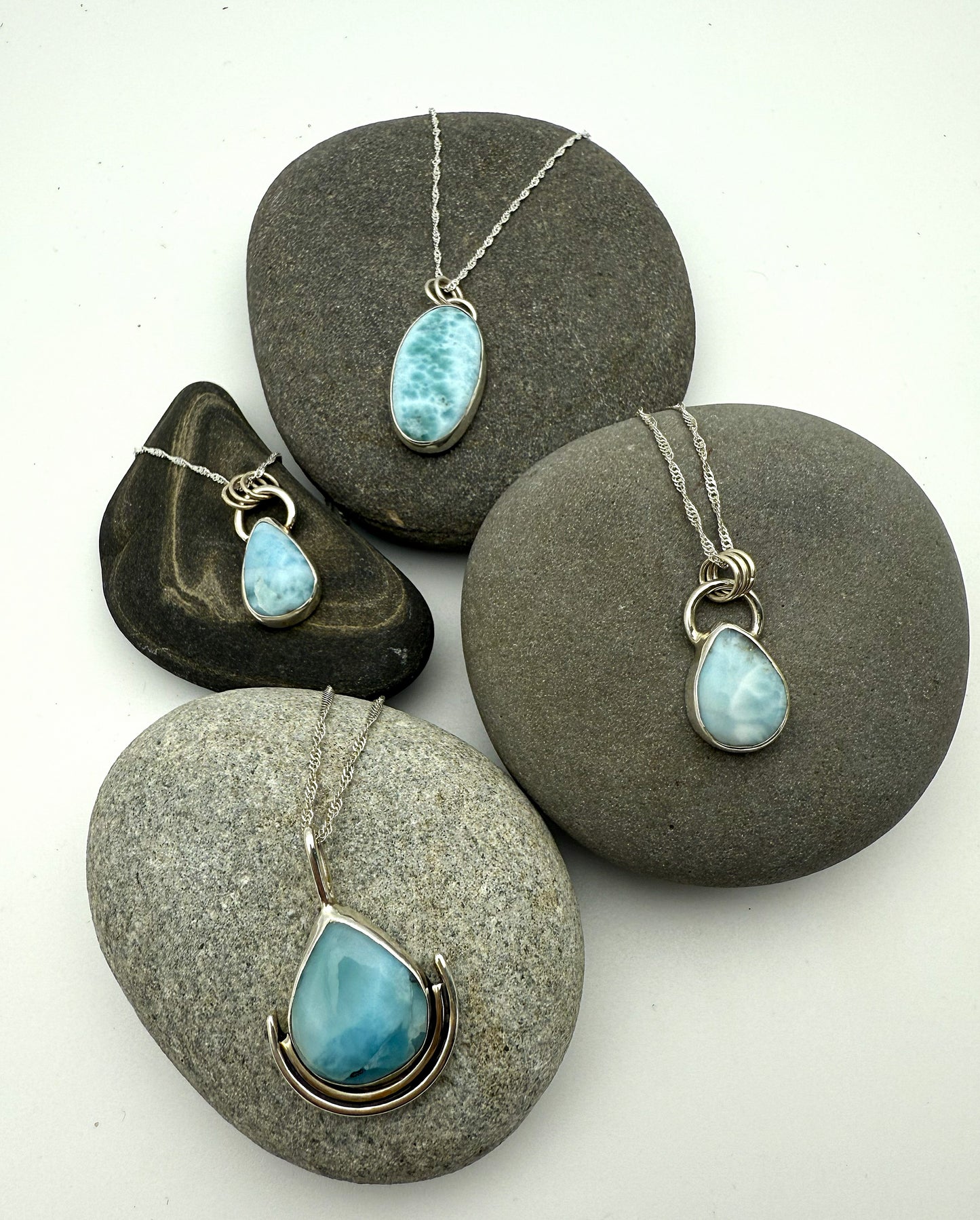 Four pendants with blue larimar  stones on grey stones against a white background