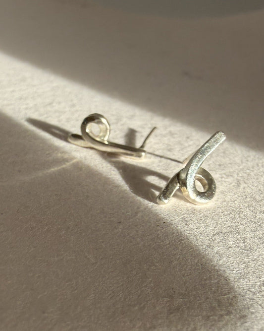 Silver brooch on a textured beige surface with soft shadows