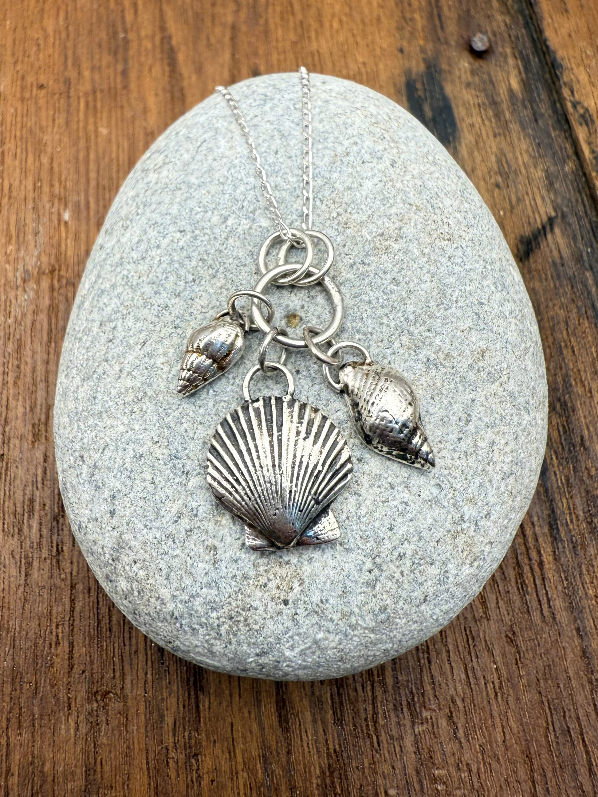 Silver necklace with shell pendants on a gray stone against a wooden background
