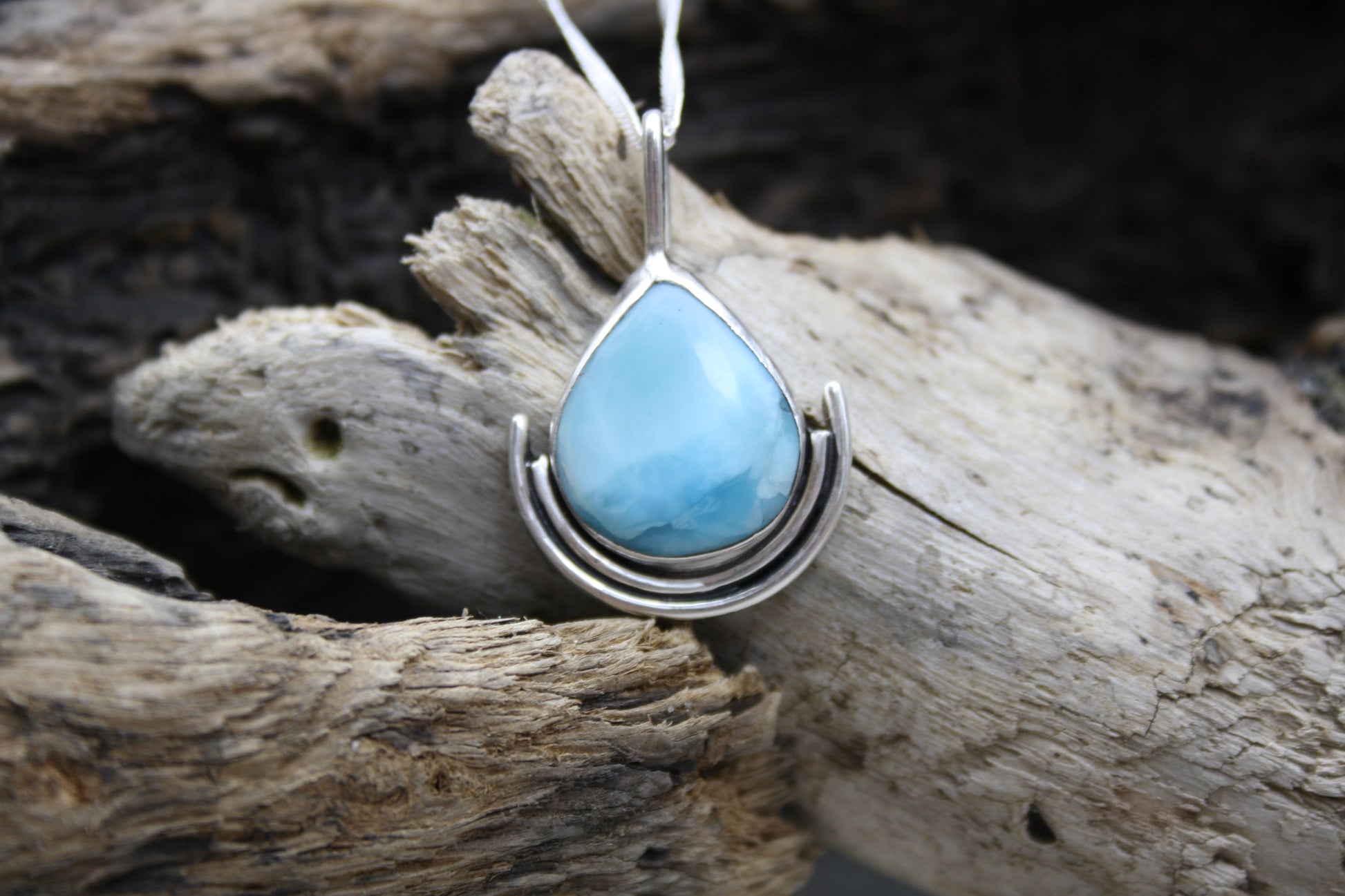 Teardrop-shaped turquoise pendant on silver chain against a wooden background
