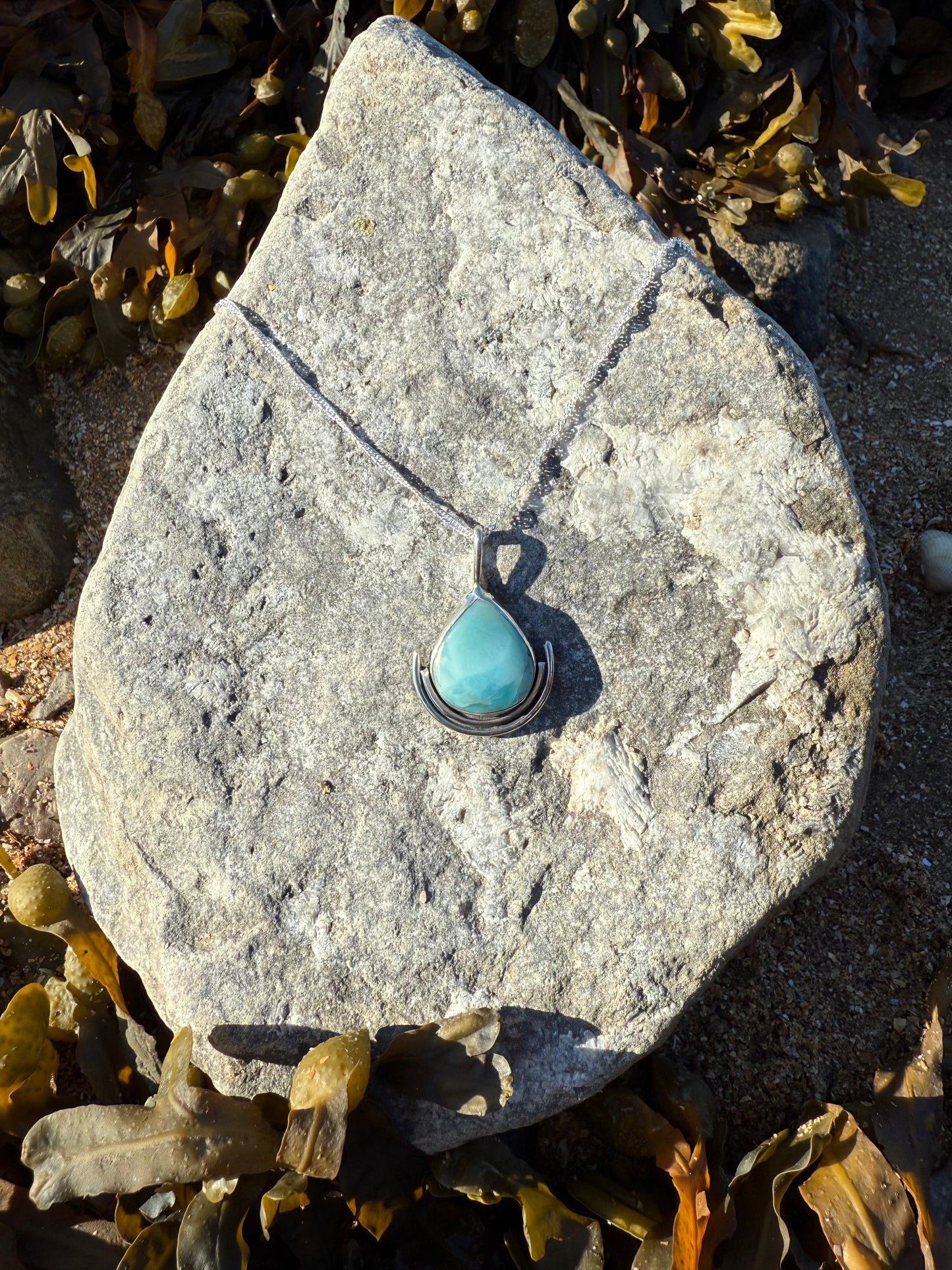 Turquoise teardrop pendant on a chain lying on a stone with seaweed around