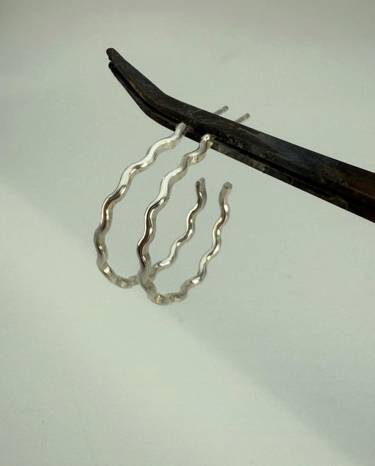 Silver wavy hoop earrings held by tweezers against a light background