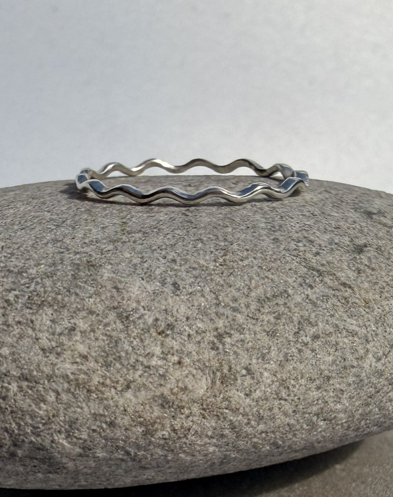 Silver wavy band ring on a gray stone with a white background
