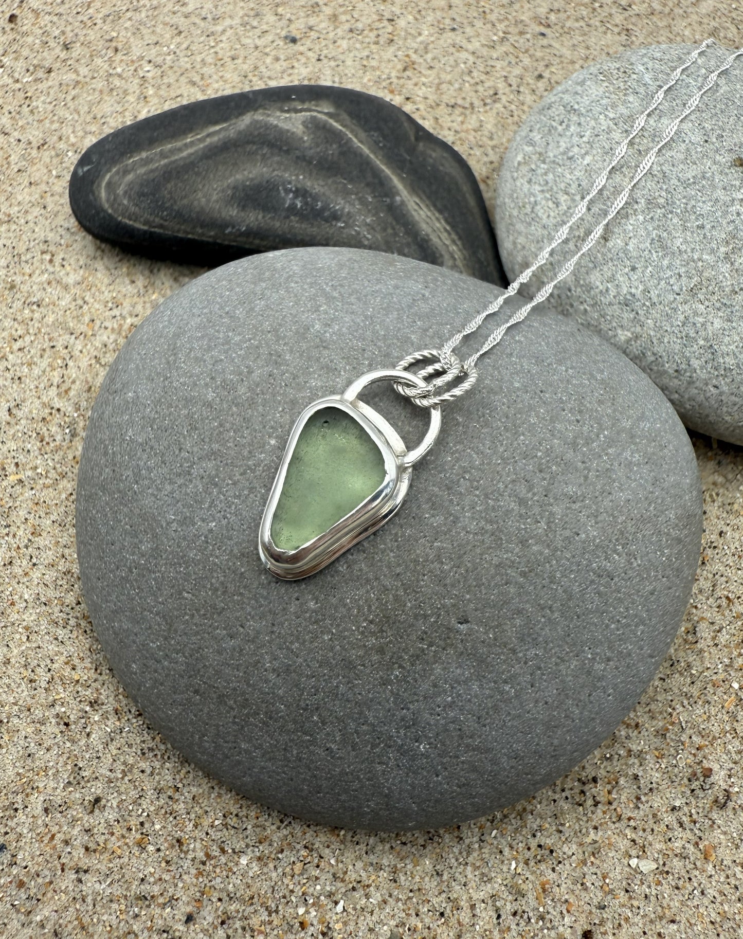 Necklace with a green sea glass pendant on a stone with a beach setting