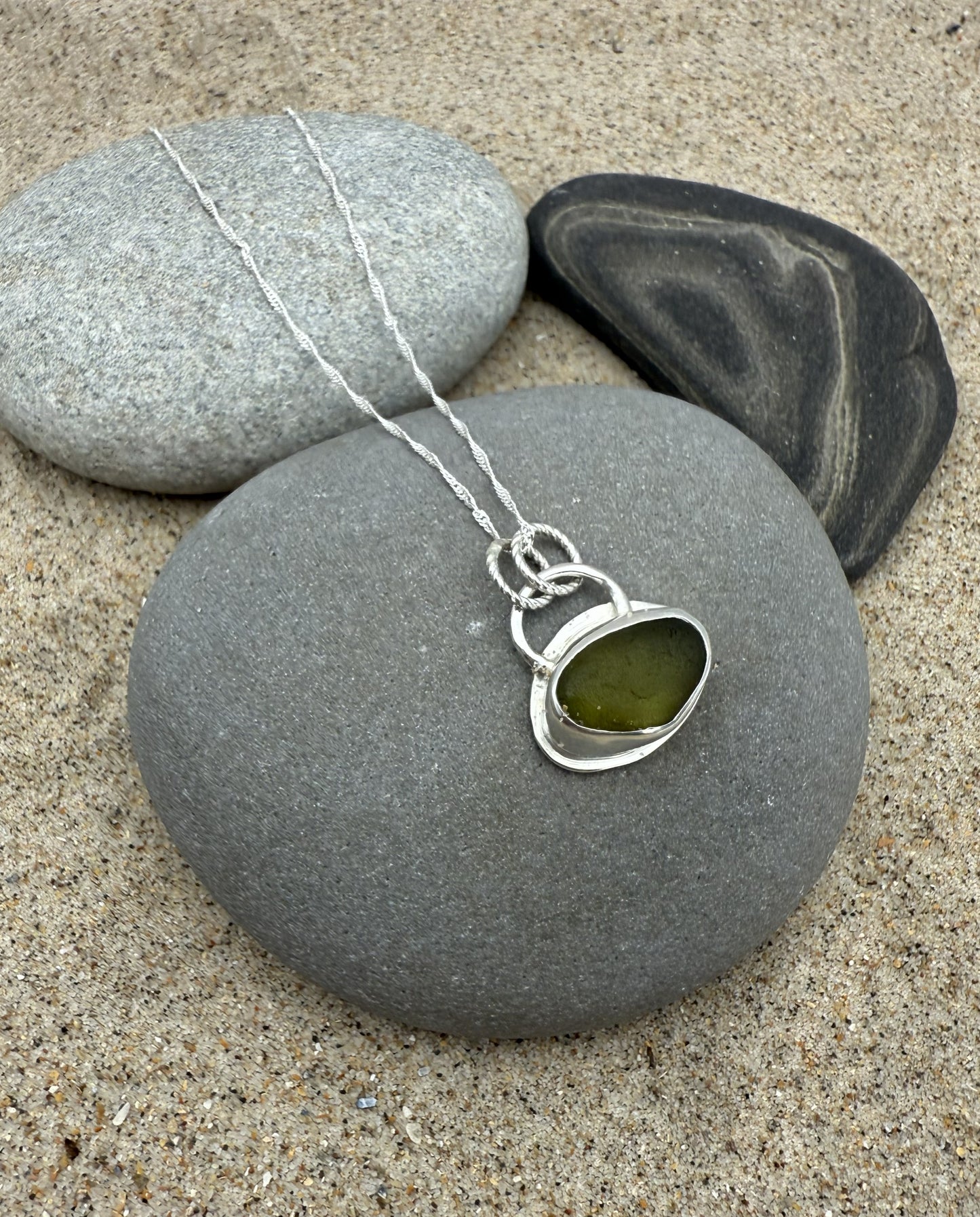 Necklace with a green stone pendant on a gray stone with sand and pebbles in the background