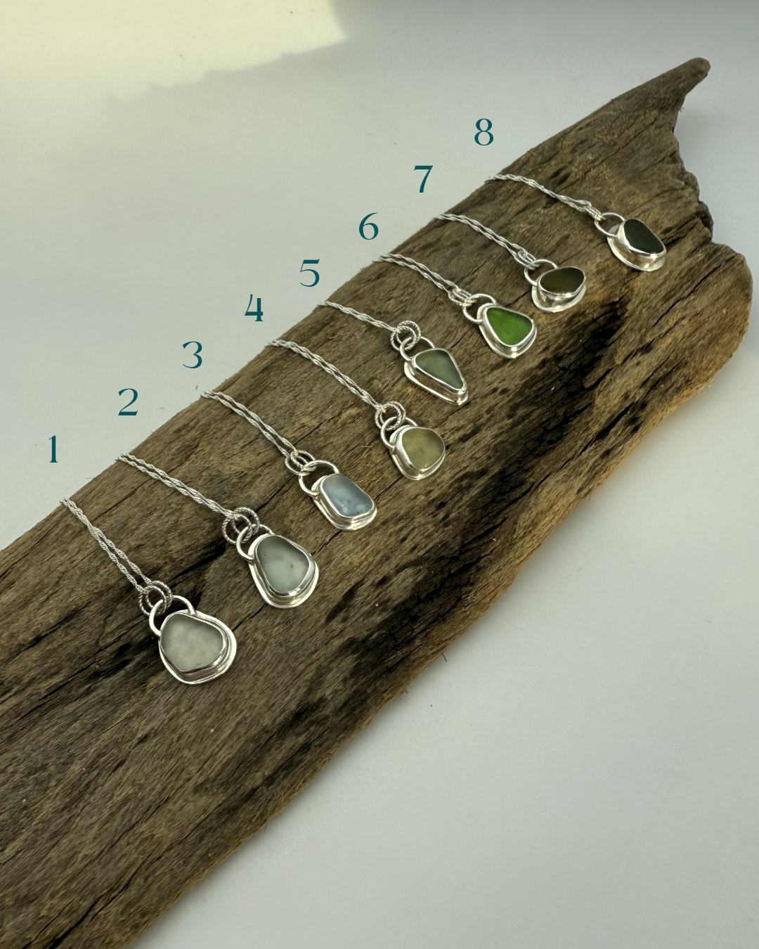 Set of silver necklaces with green and clear stone pendants on a wooden block.