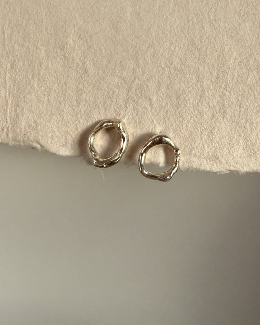 Small silver molten organic stud earrings on a textured beige surface