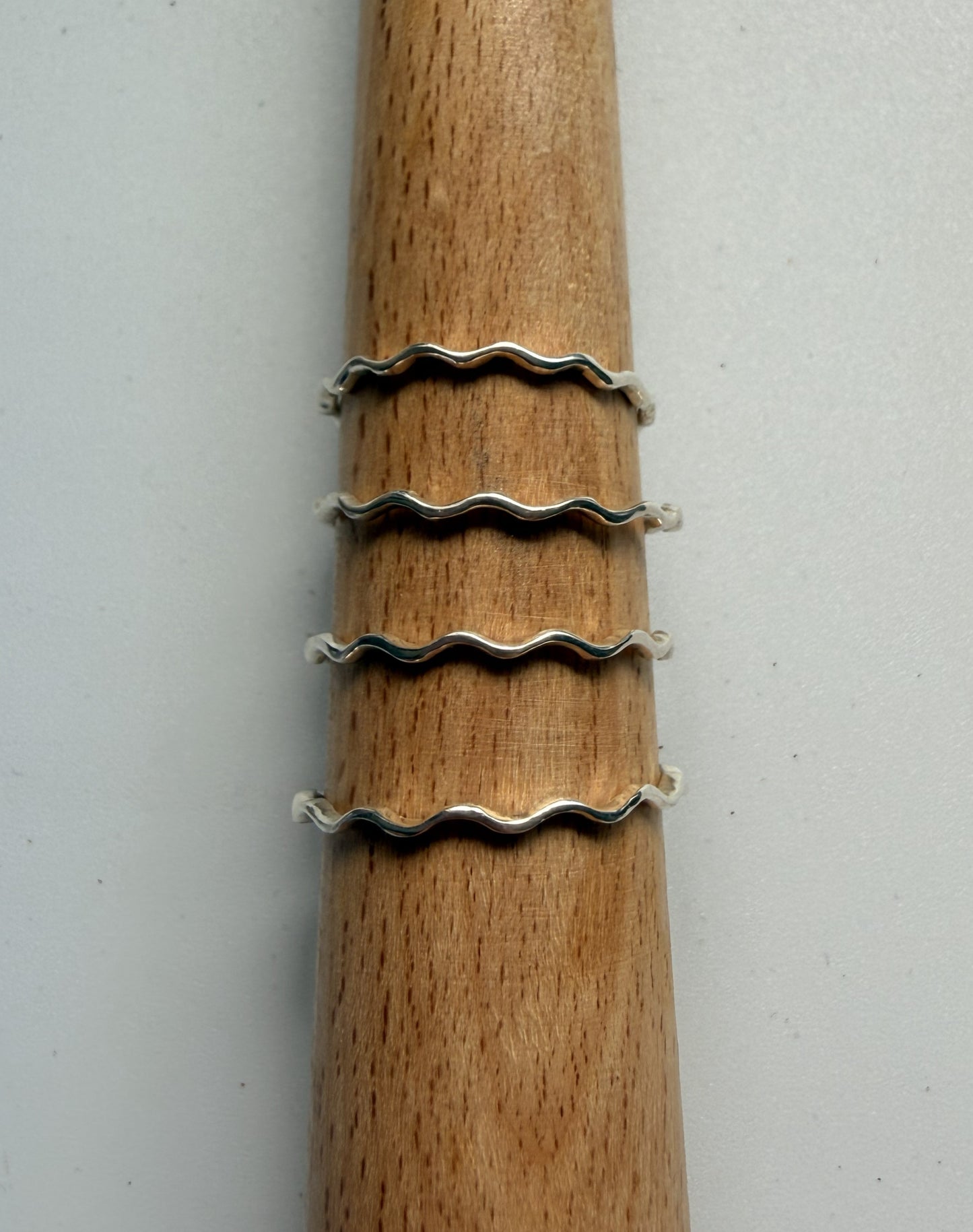 Silver wavy rings stacked on a wooden stick against a white background