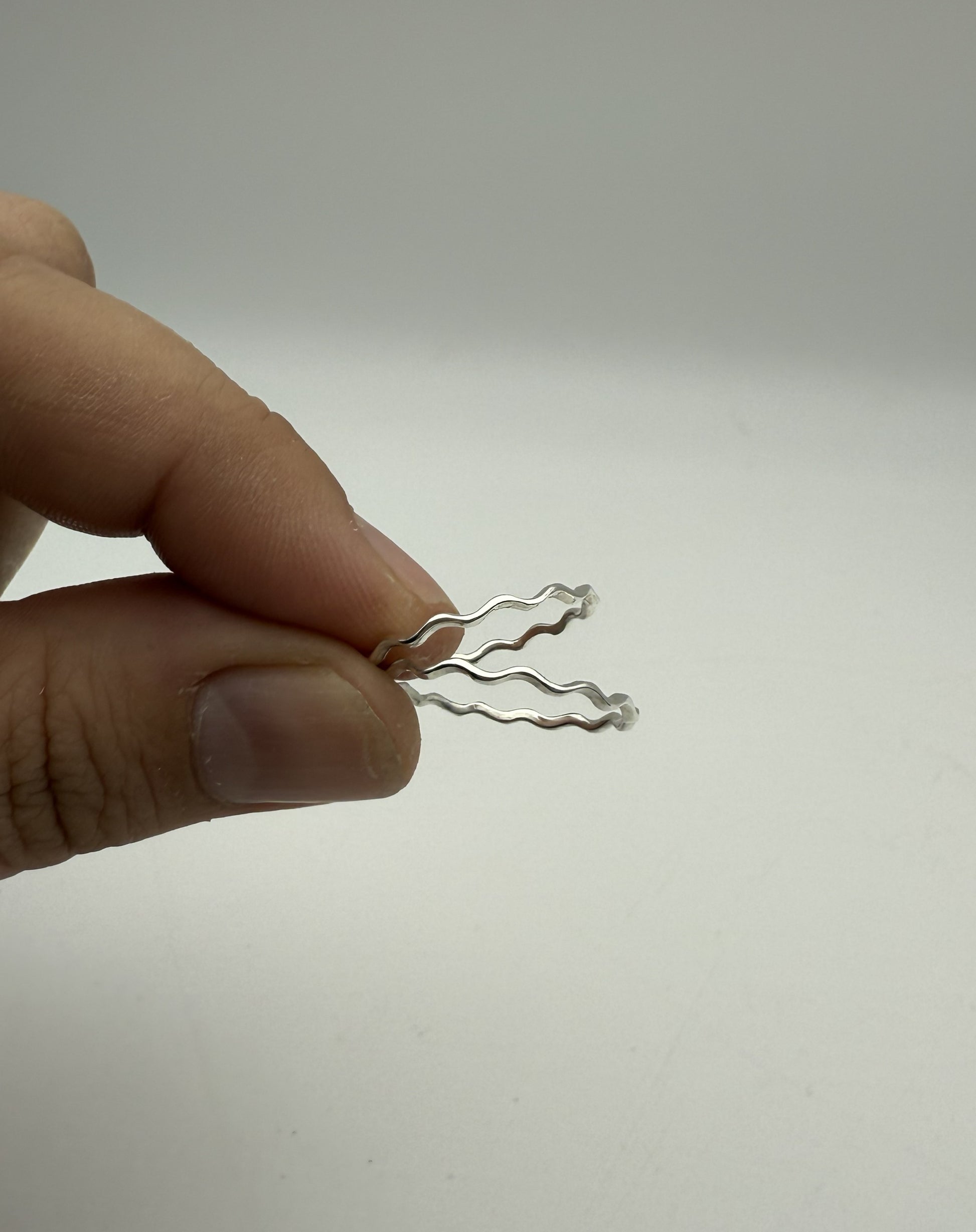 Silver wavy rings held between fingers against a plain background