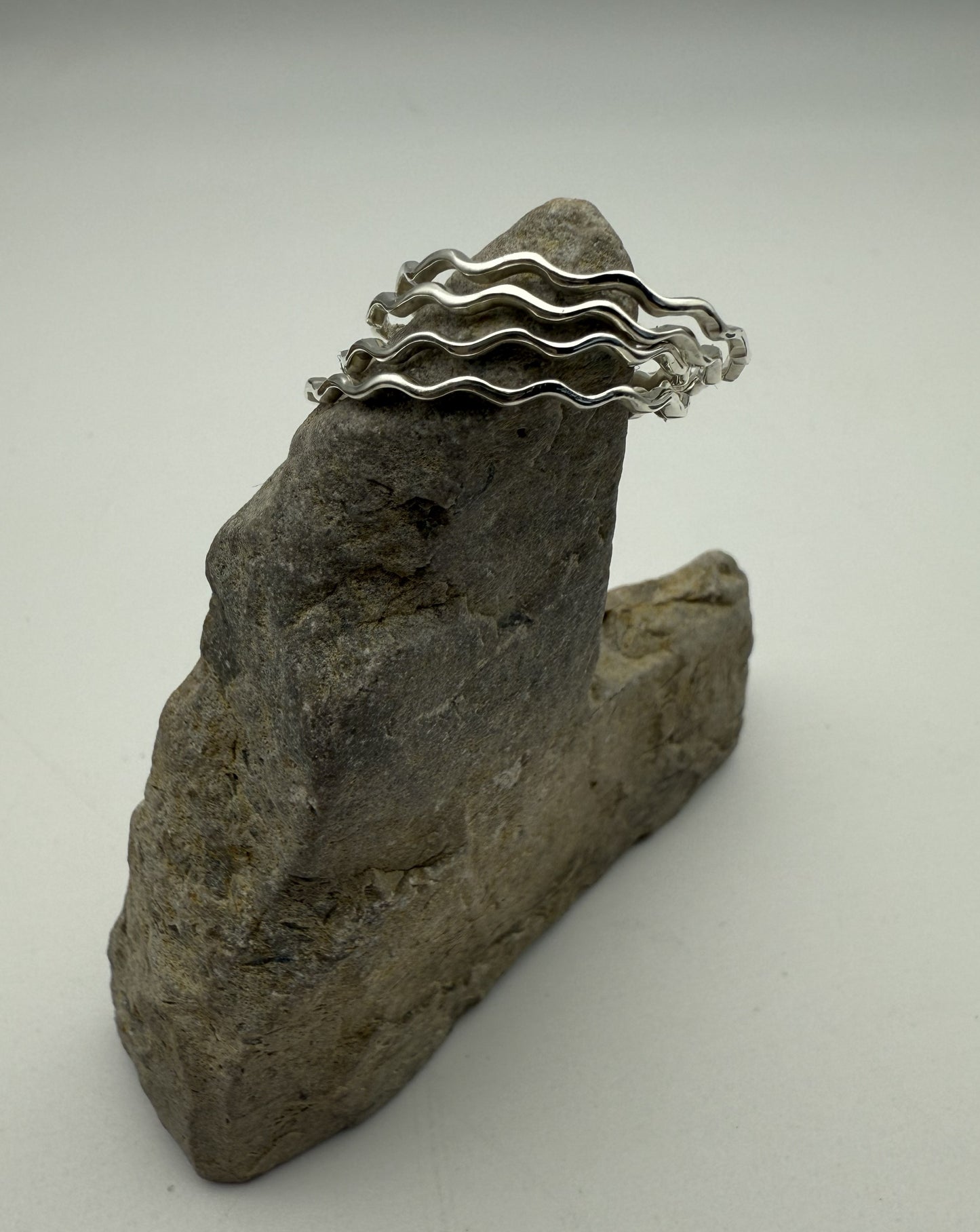 Silver wavy rings on a rock with a white background