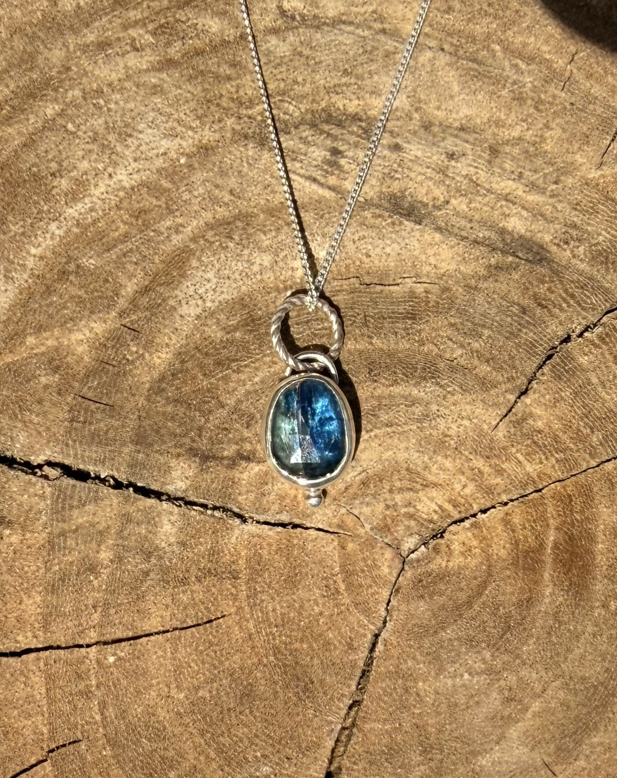 Silver kyanite necklace with a blue pendant on a wooden surface