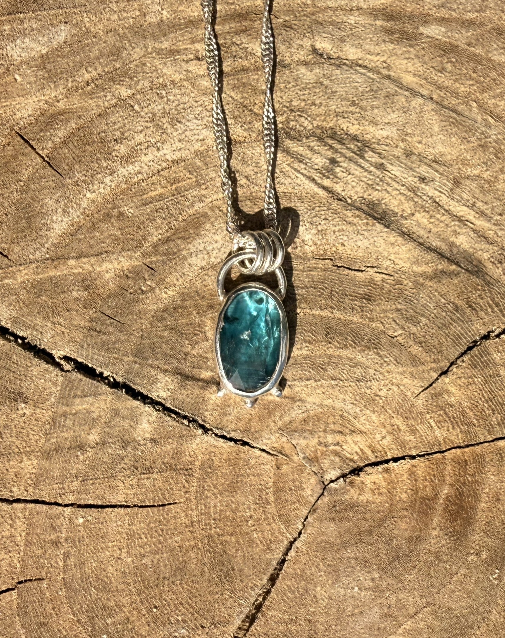 Teal kyanite stone pendant on a silver chain against a wooden background