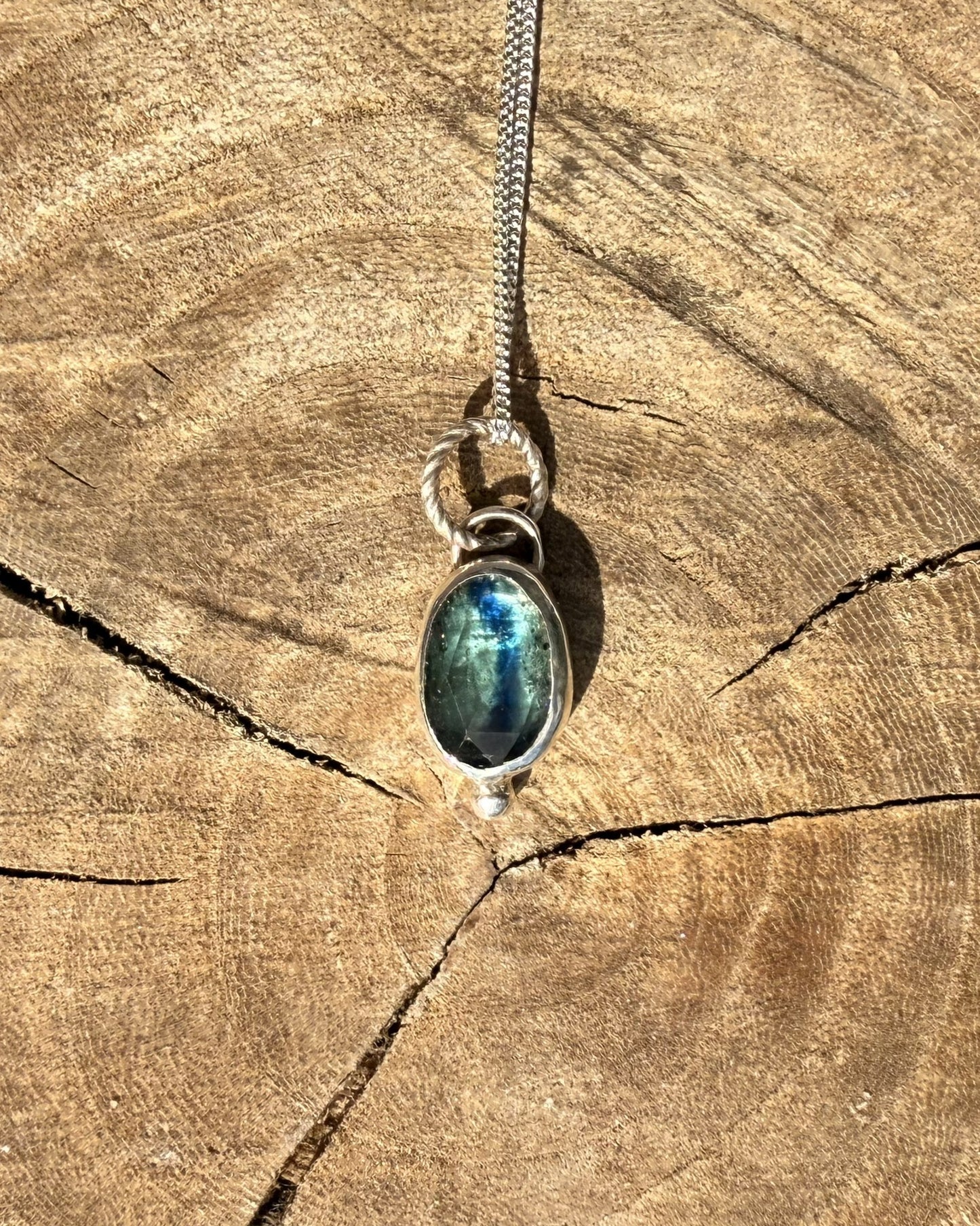 Necklace with a pendant featuring a blue kyanite stone on a wooden surface