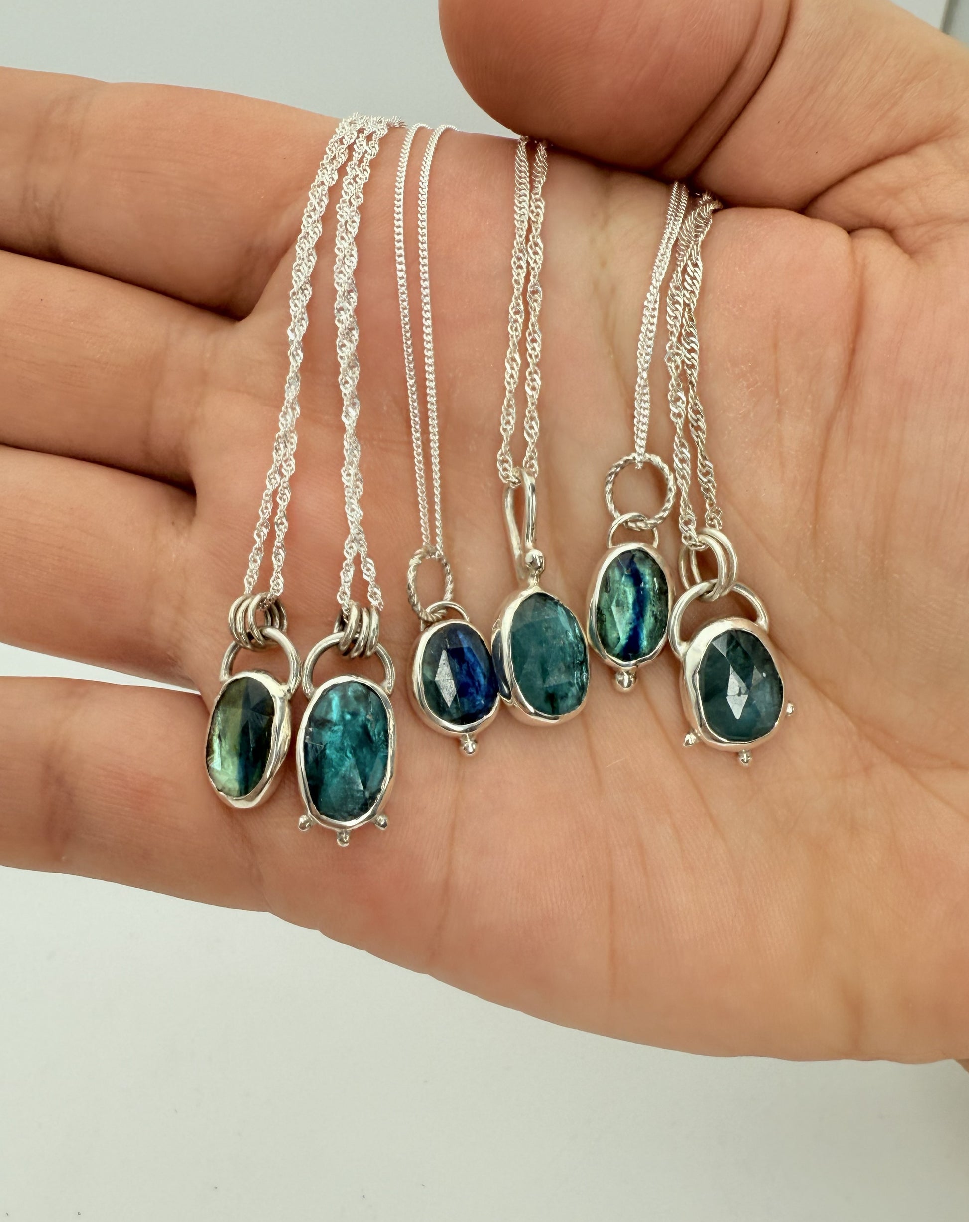 Silver necklaces with blue kyanite gemstones held in a hand against a neutral background