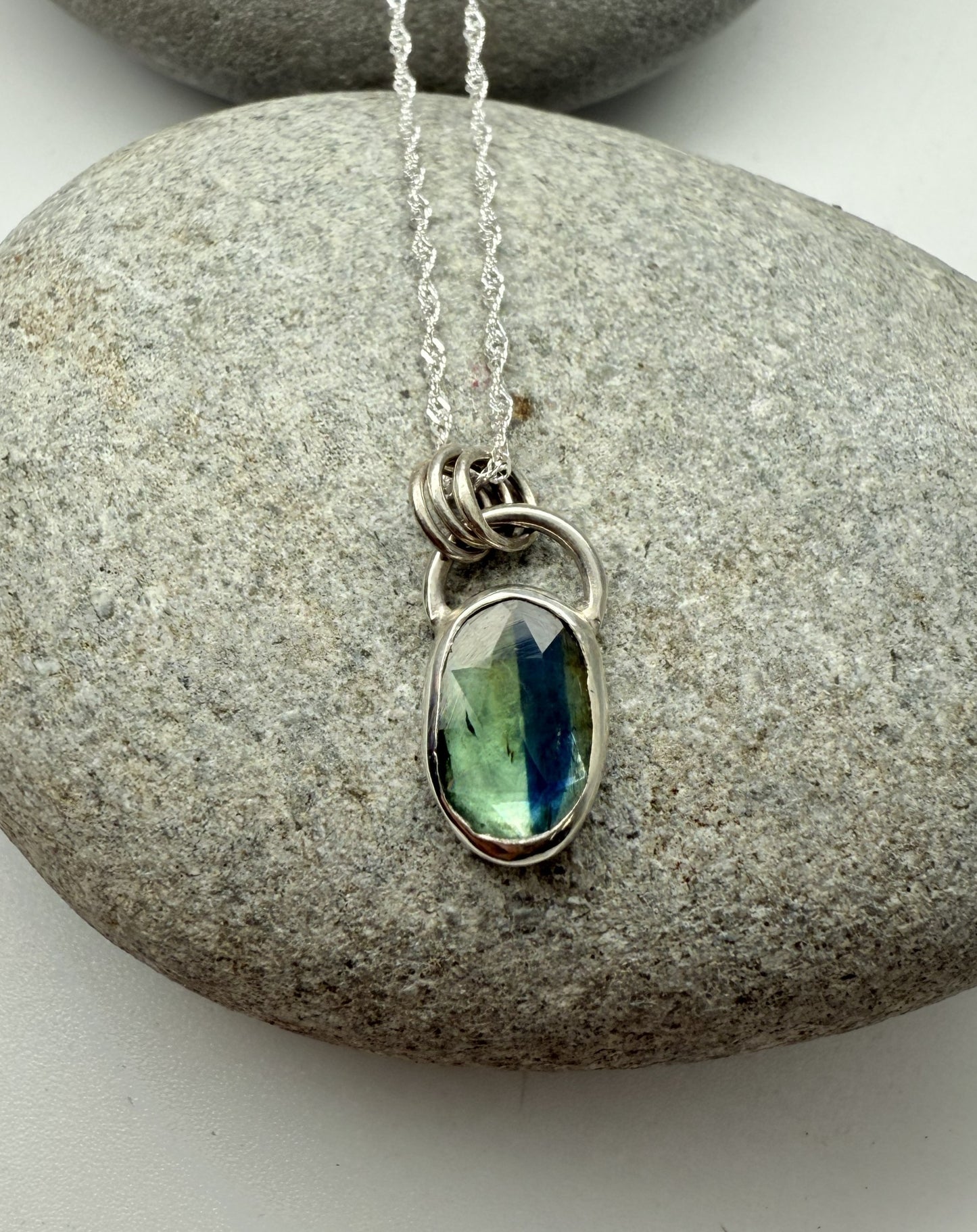 Necklace with a green kyanite gemstone pendant on a stone surface