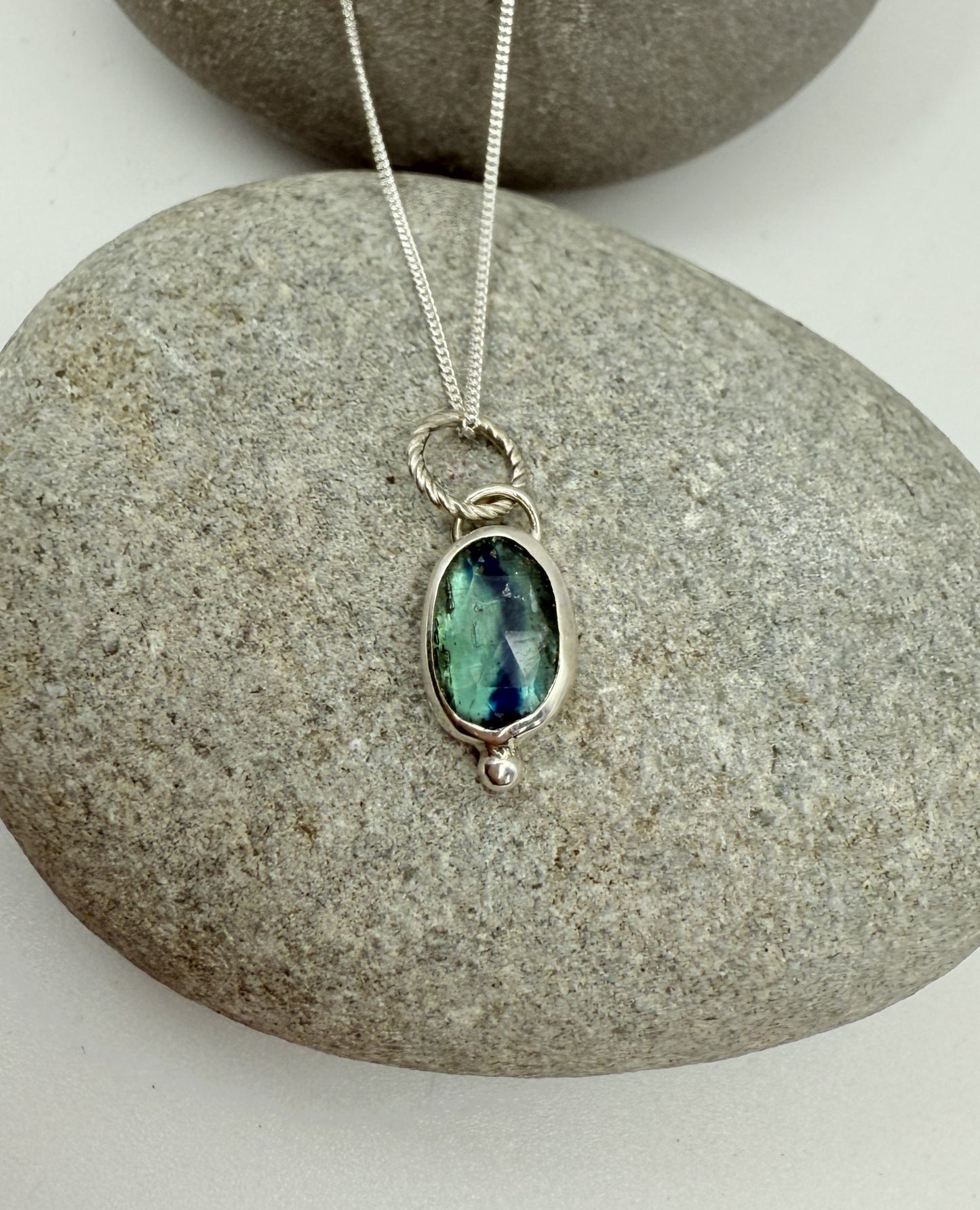 Silver necklace with a green kyanite gemstone pendant on a stone surface