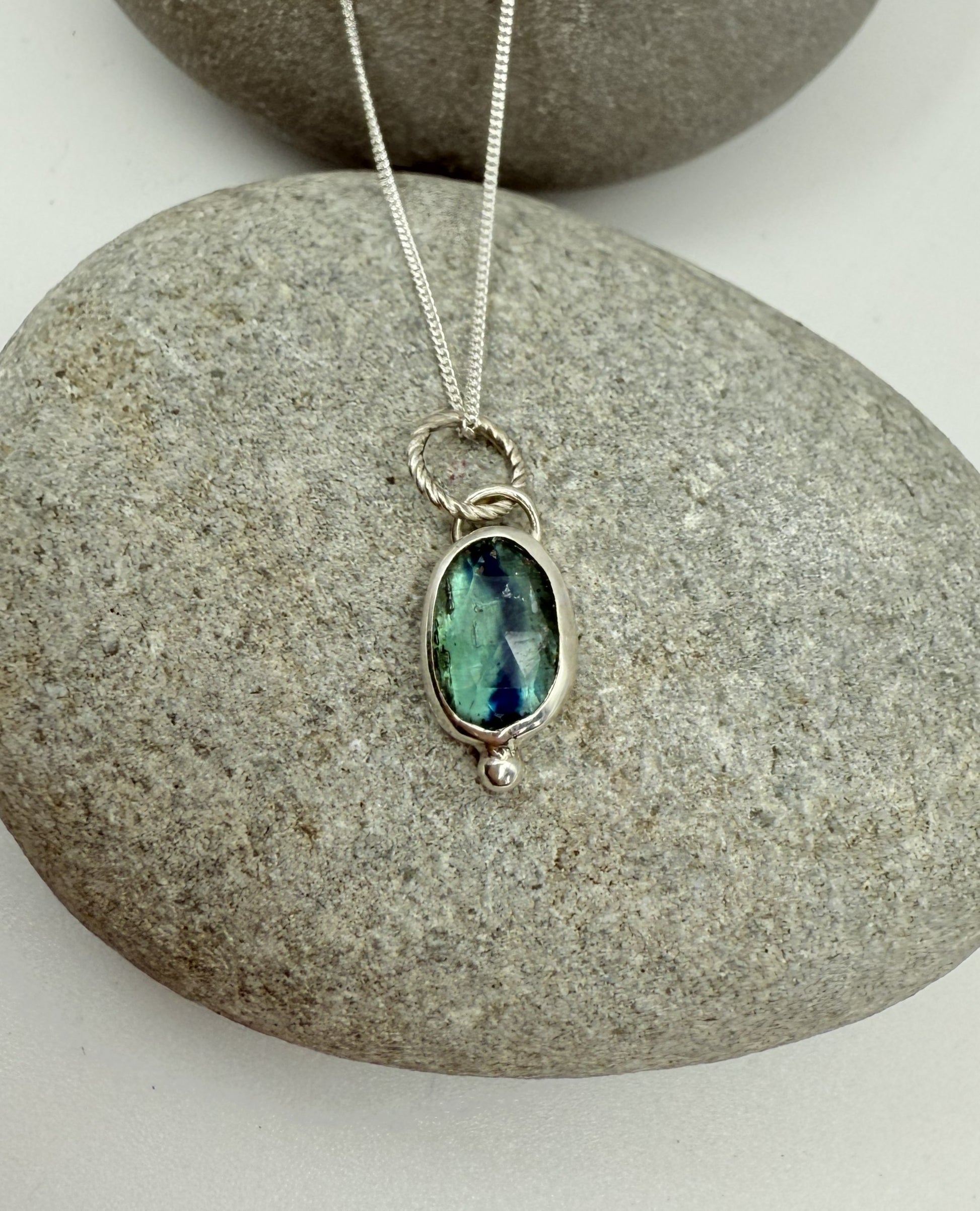 Silver necklace with a green kyanite gemstone pendant on a stone surface