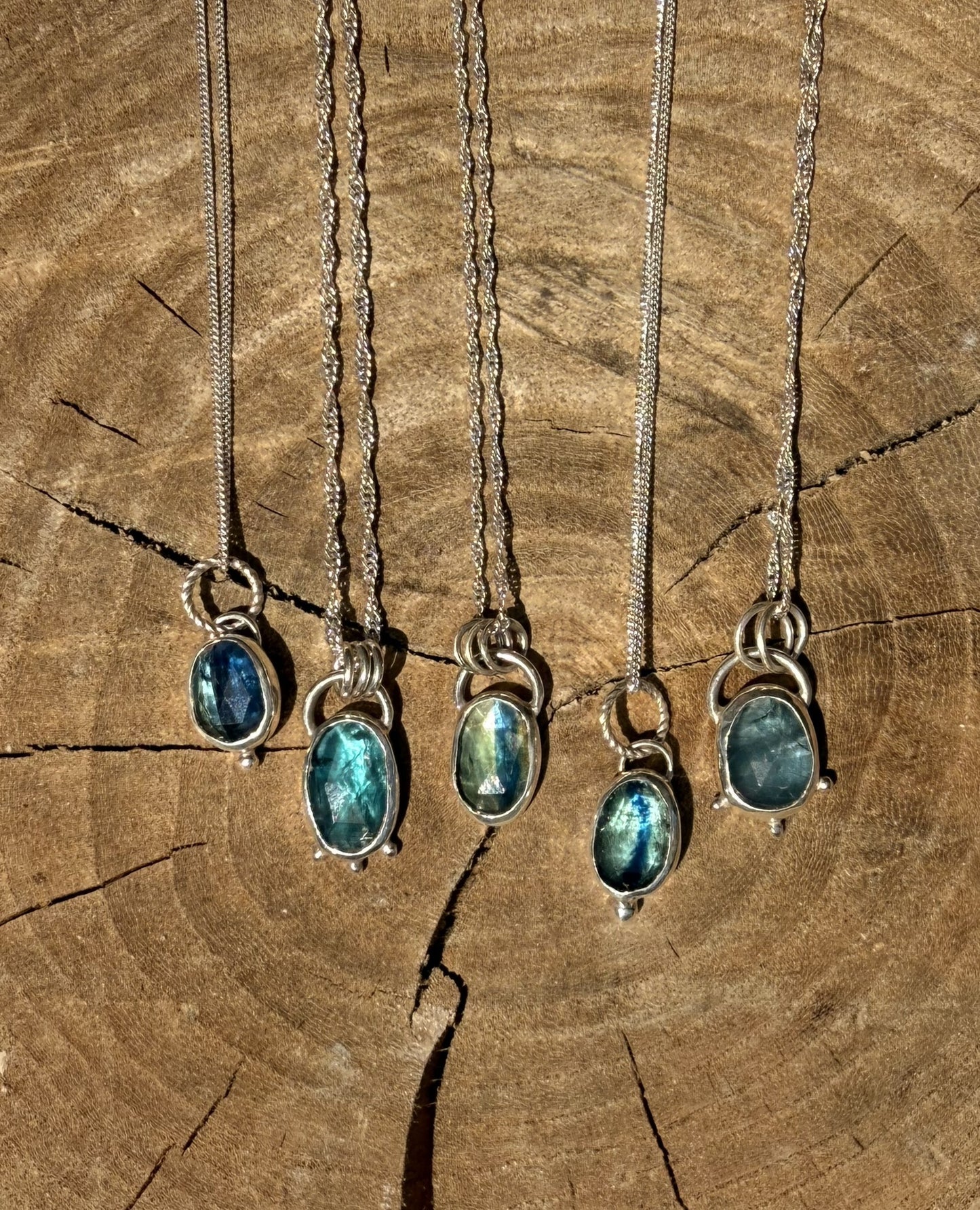 Five silver necklaces with kyanite gemstone pendants on a wooden surface