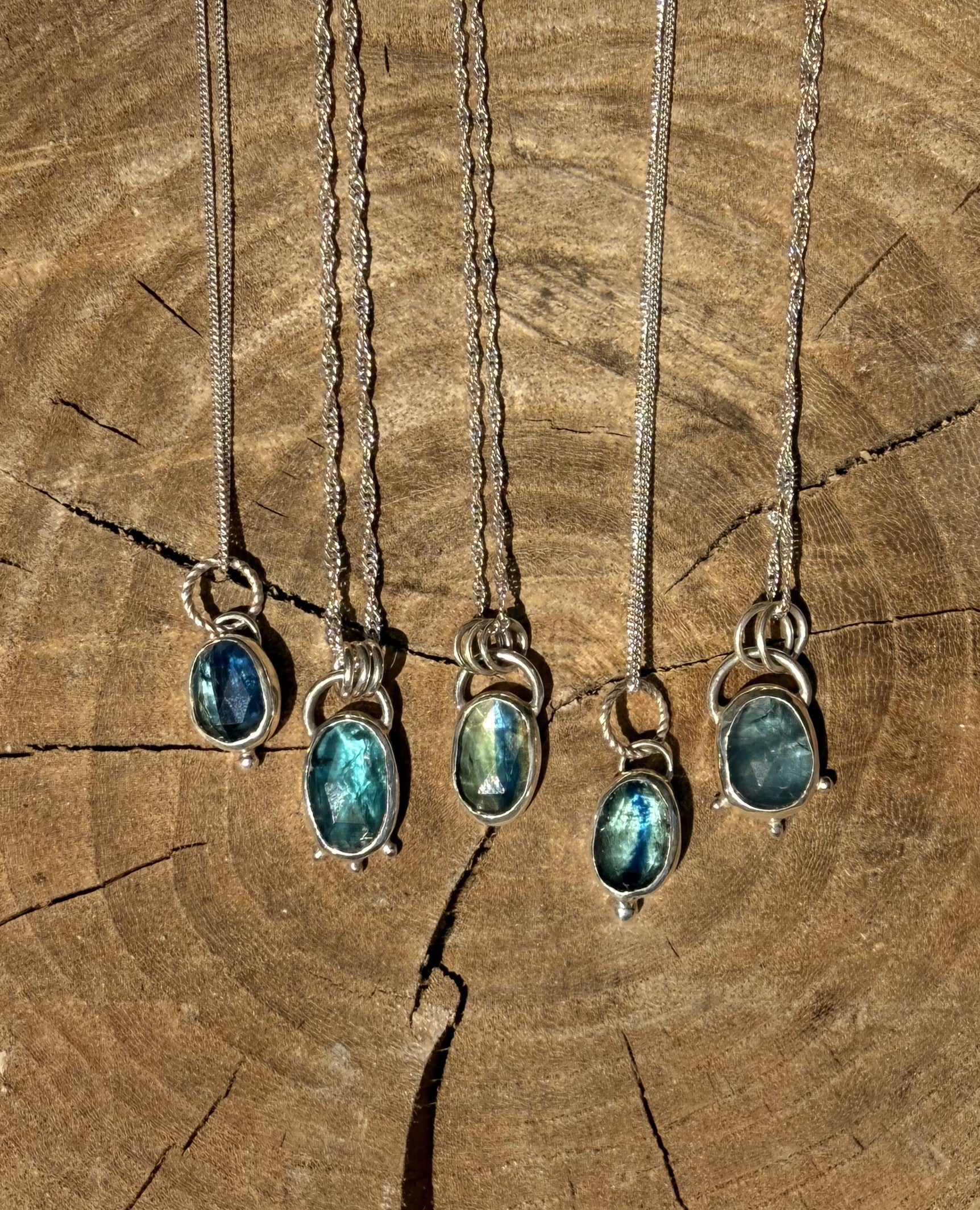 Five silver necklaces with kyanite gemstone pendants on a wooden surface