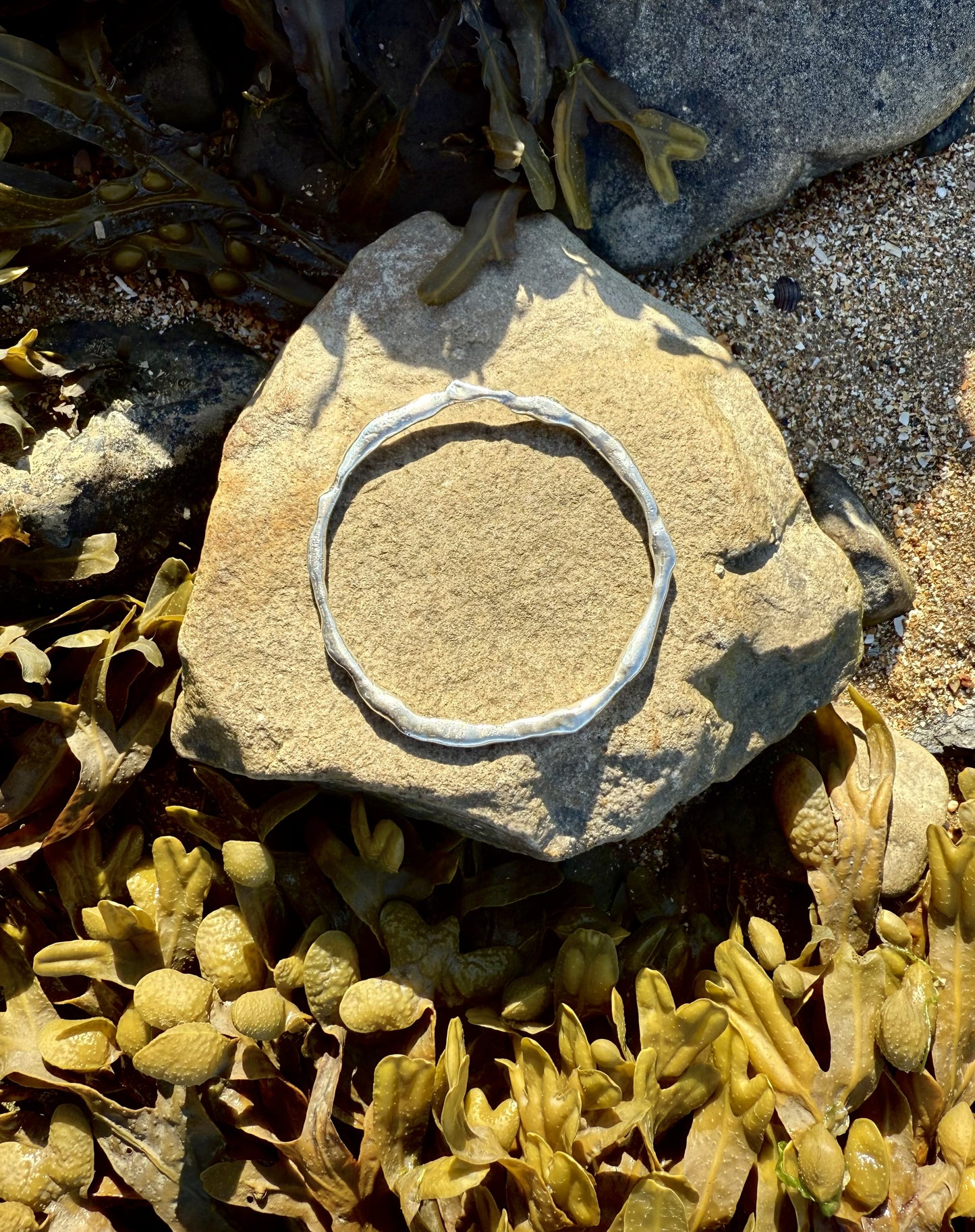 Silver bangle on a stone with seaweed and sand in the background