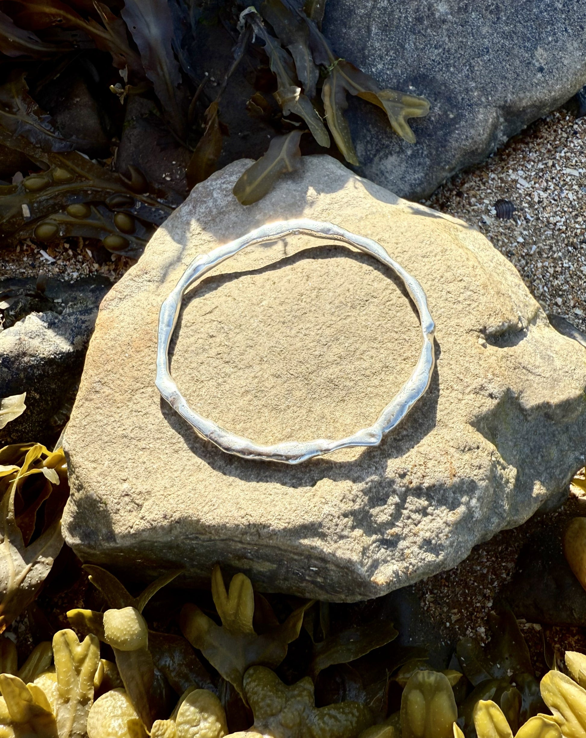 Silver bracelet on a stone with seaweed and rocks in the background