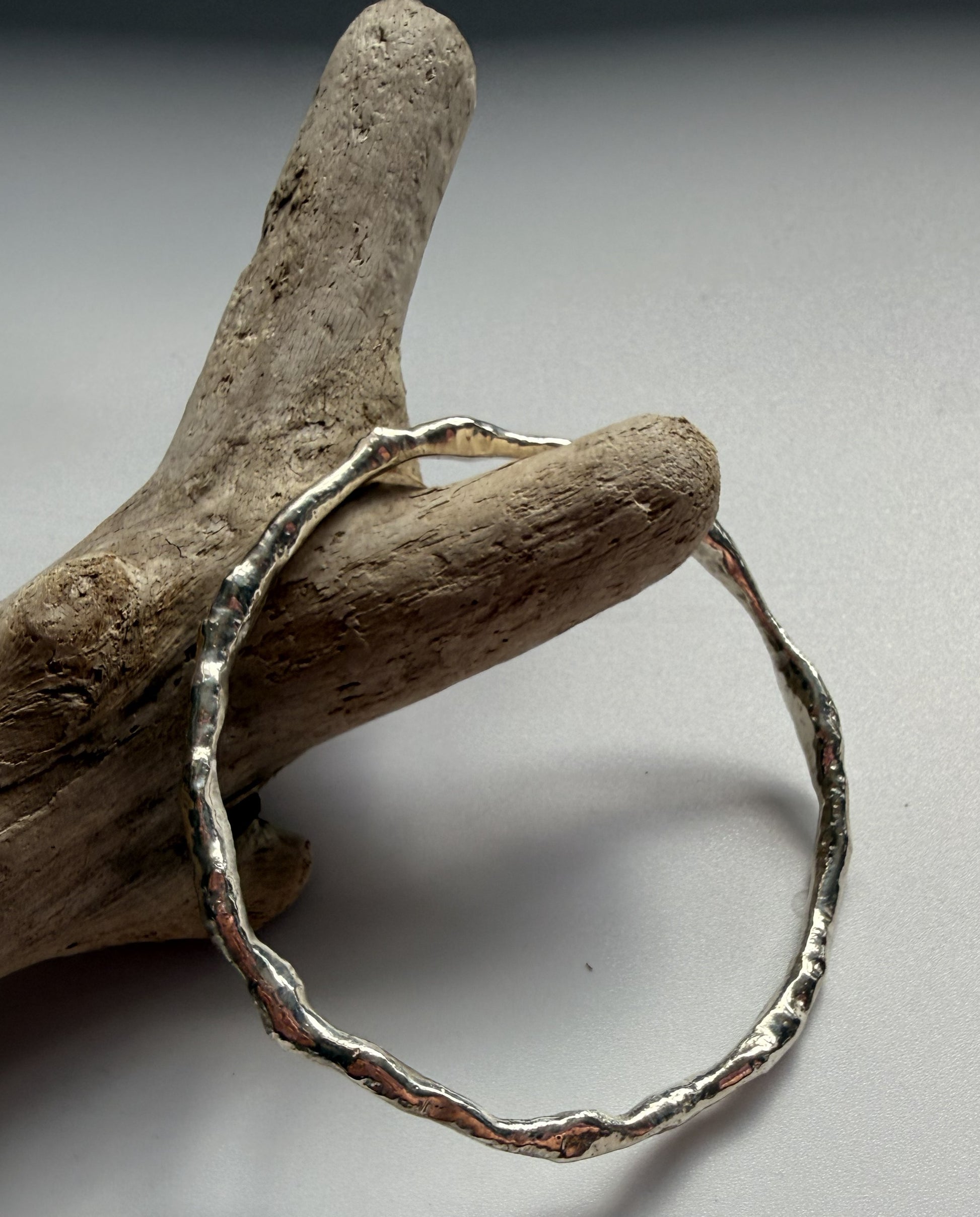 Silver bracelet on a piece of driftwood against a grey background