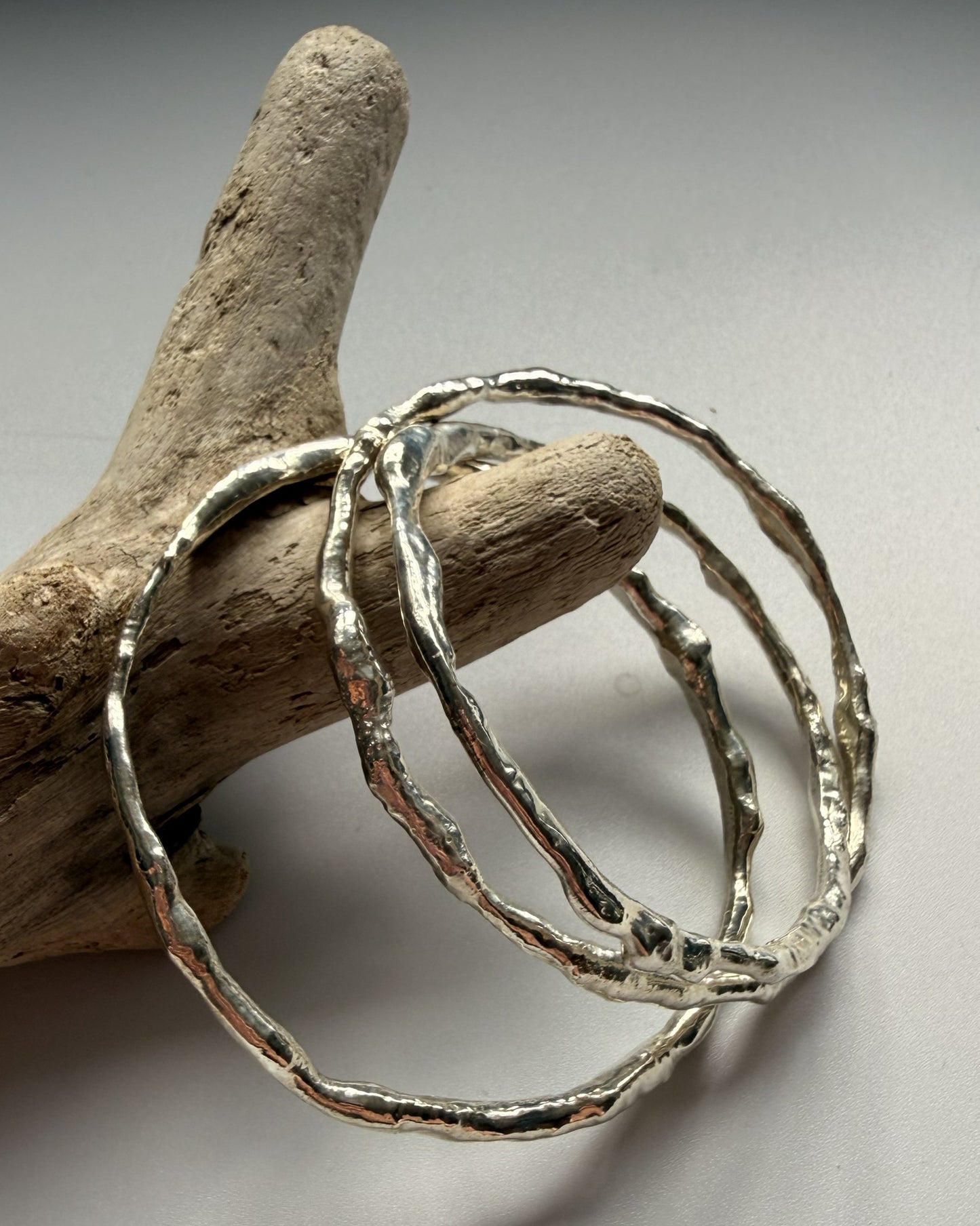 Silver bangles on a piece of driftwood against a neutral background